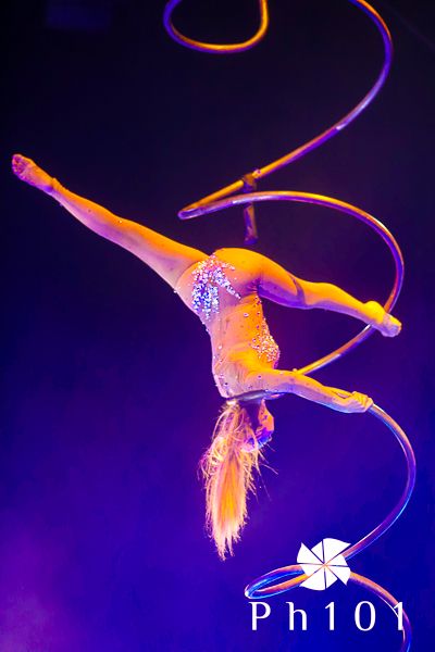 Dramatic aerial acrobatic performance with orange and purple lighting effects on dark background.