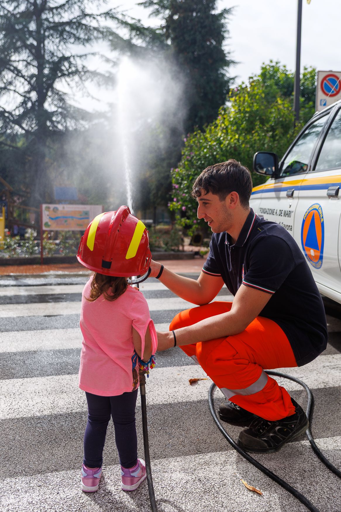 Children learning about fire safety and water hoses in a parking lot.