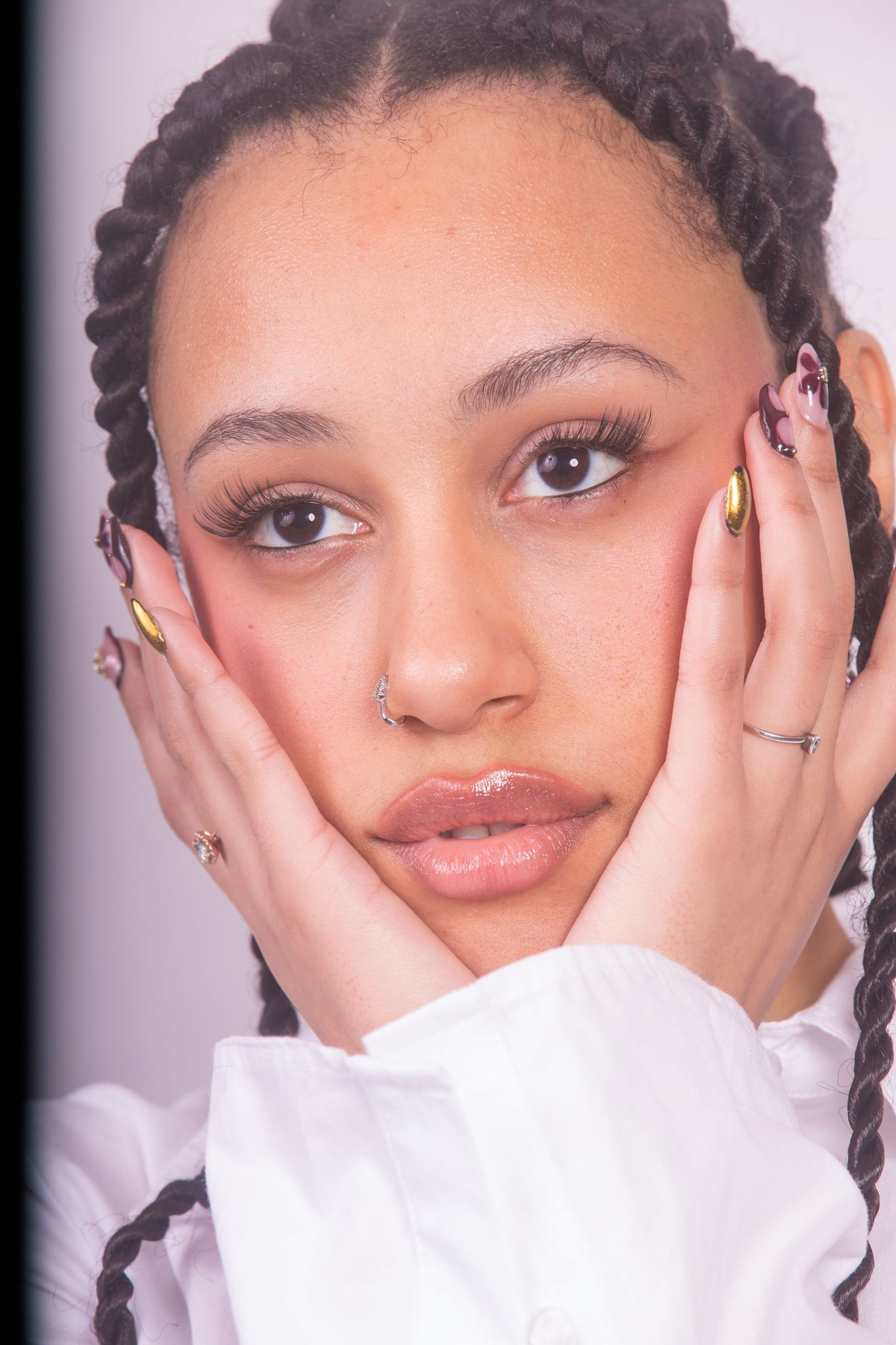 Close-up beauty portrait with braided hair and white collar against neutral background.