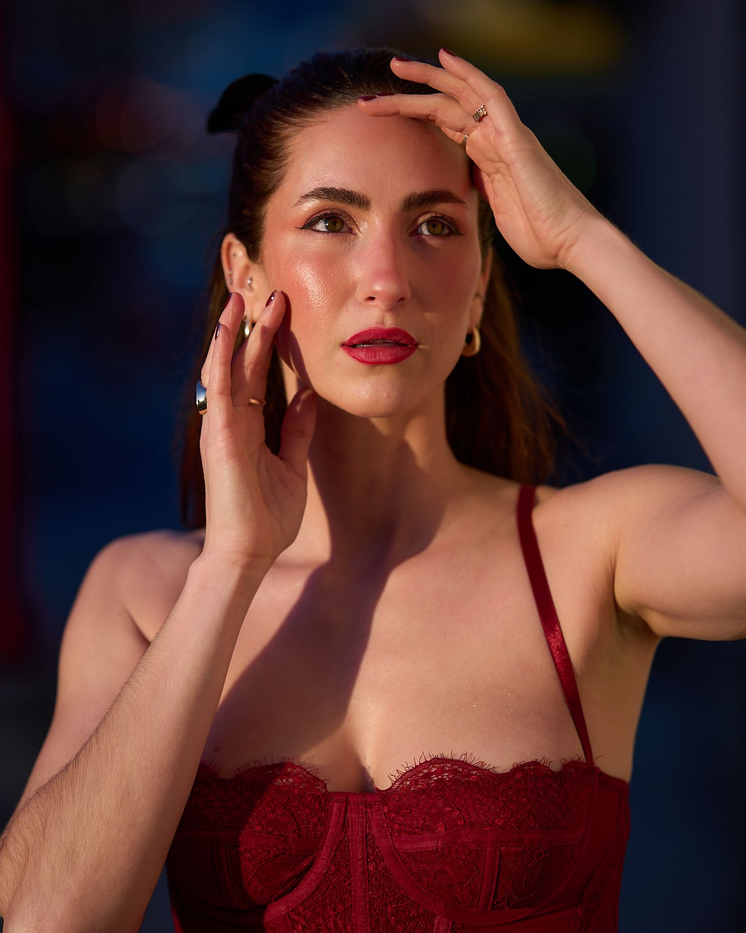 Dramatic portrait with hands raised against dark blue background.