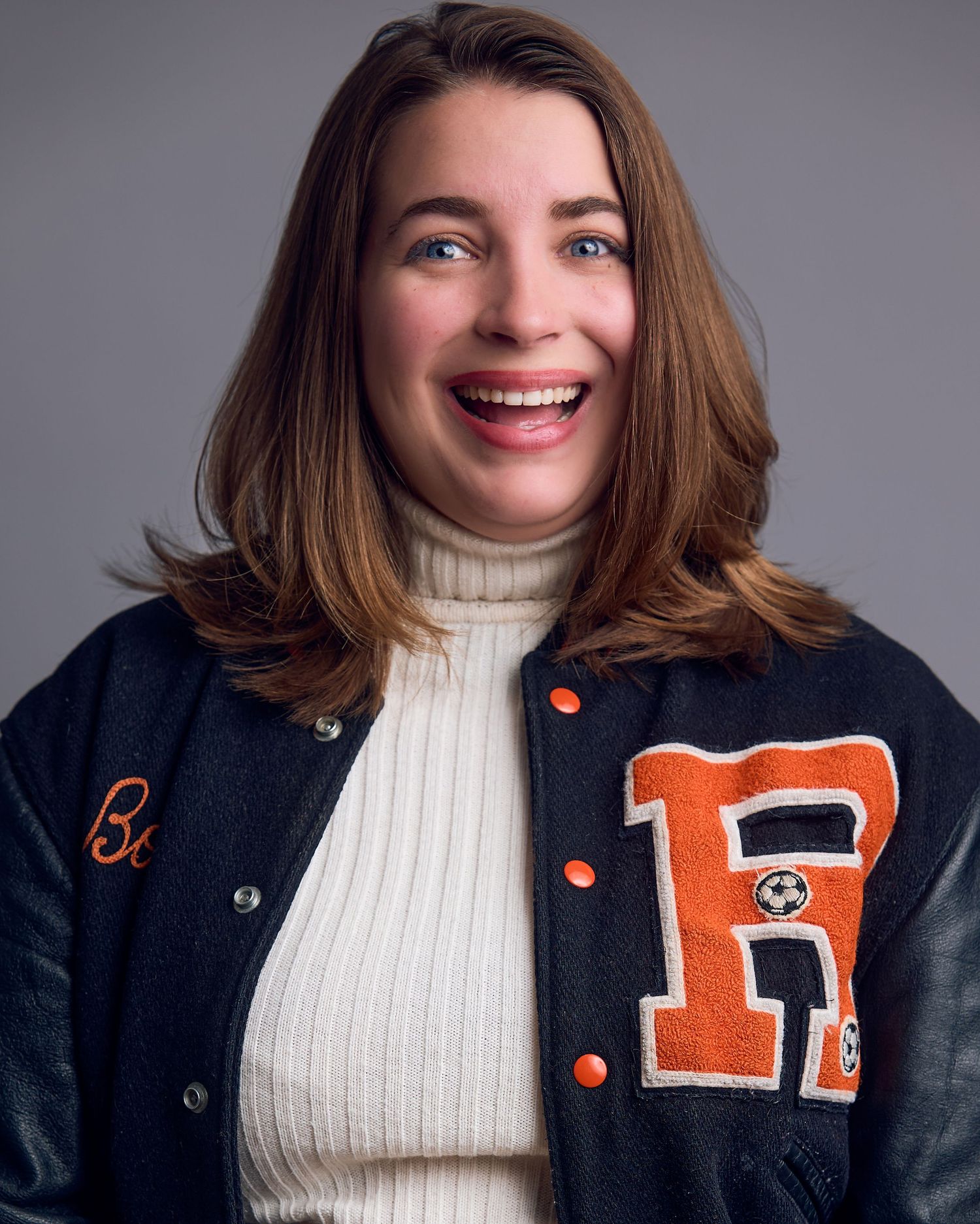 Portrait series in cream turtleneck and navy varsity jacket with orange letter.