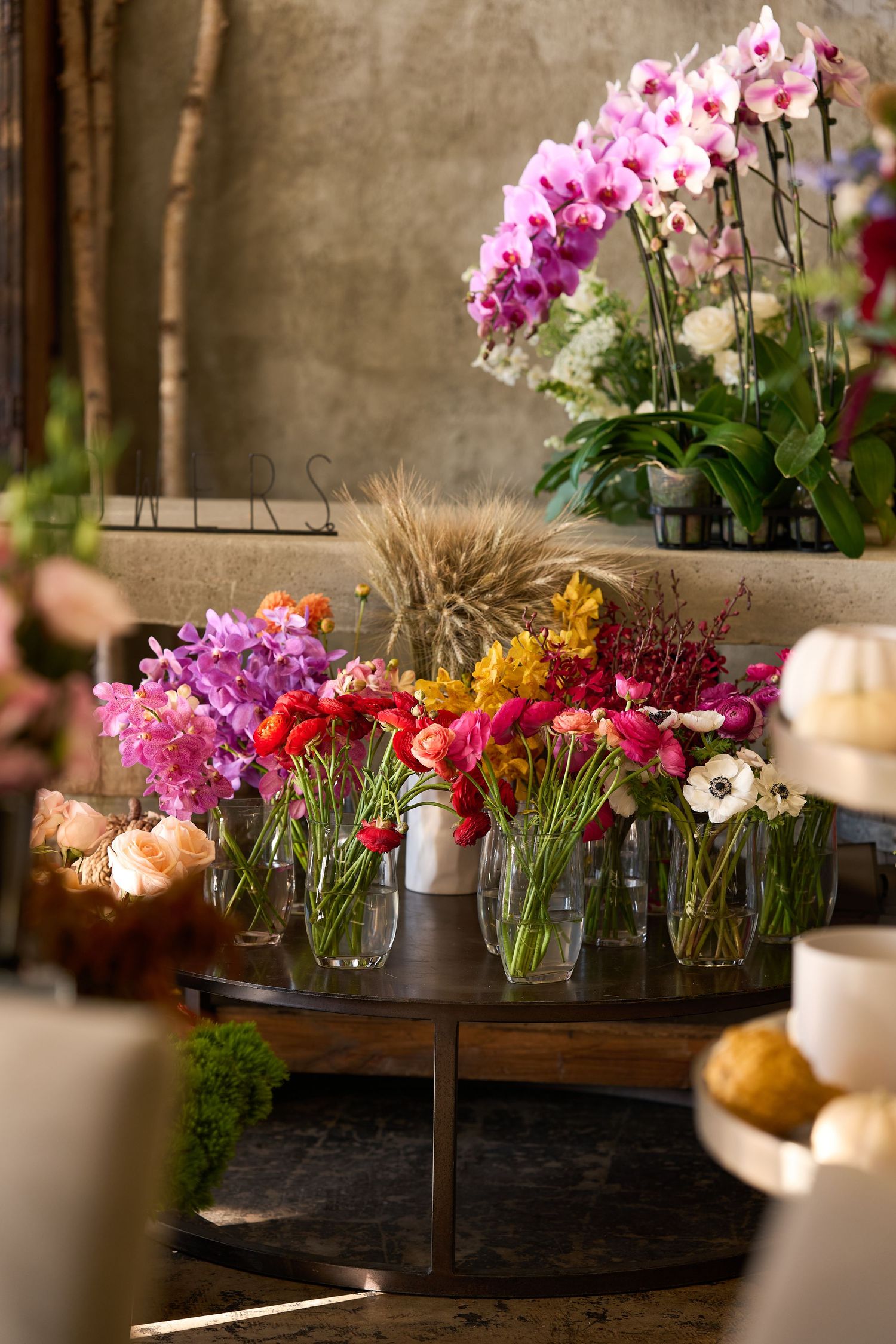Beautiful floral arrangement with pink orchids and white flowers in glass vases on a rustic wooden table with candlelight.