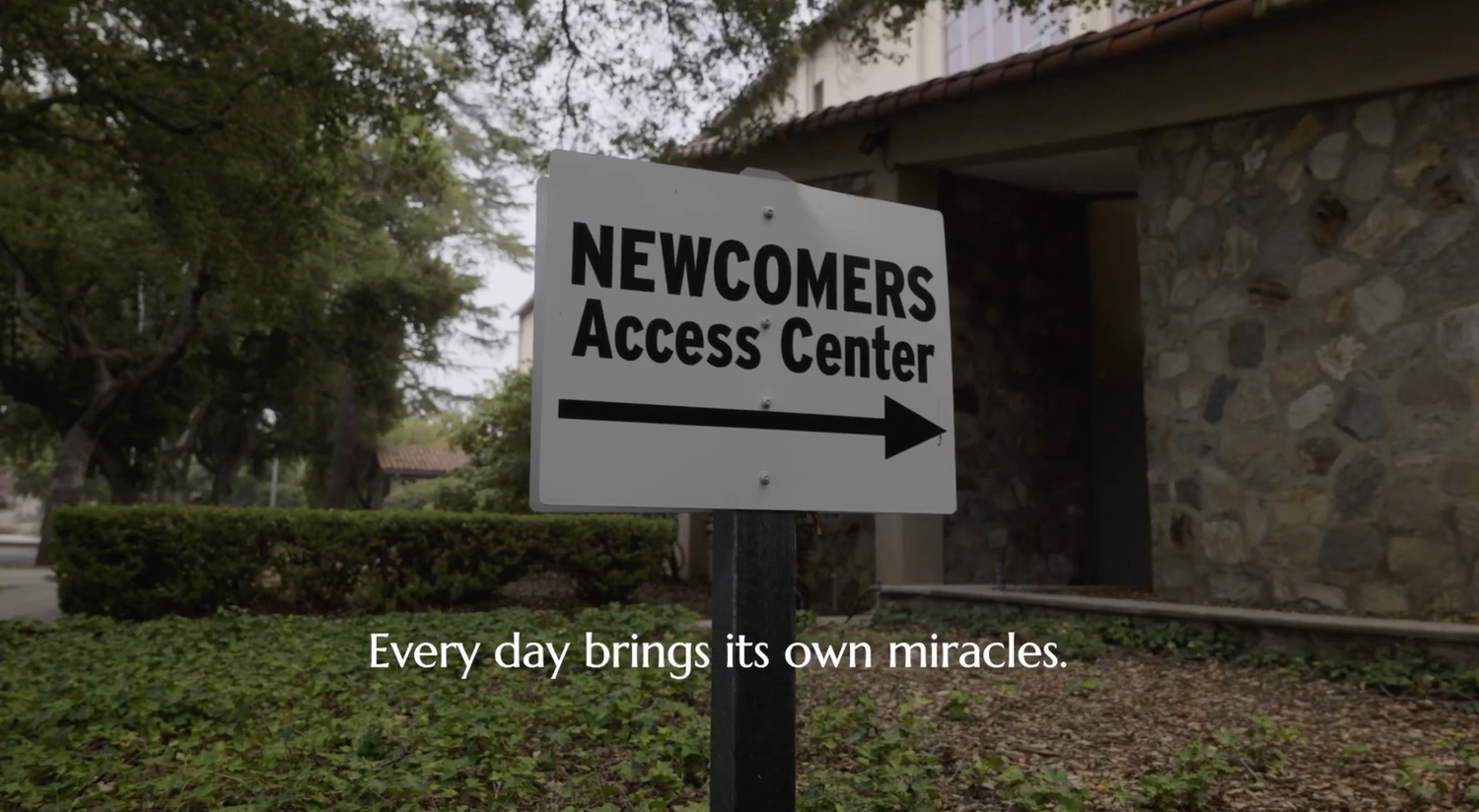 A directional sign for 'Newcomers Access Center' with an arrow pointing right and an inspirational quote below.