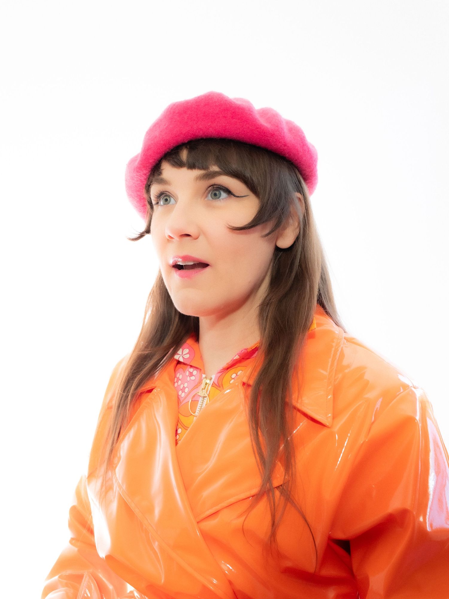 Young woman wearing a bright pink beret and orange vinyl raincoat against a white background.