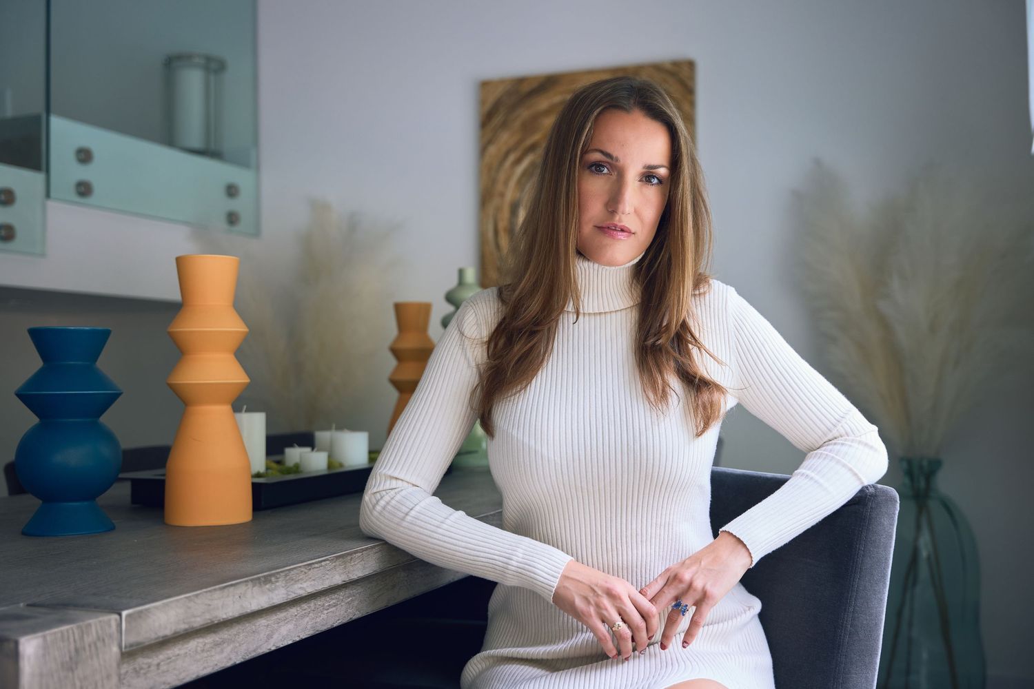 Minimalist portraits in white turtleneck against modern interior with decorative vases.