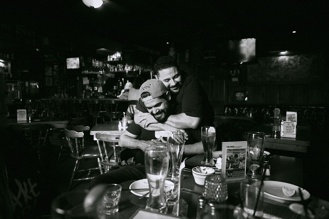 Two people sharing a warm hug at a dimly lit bar in a black and white photo.