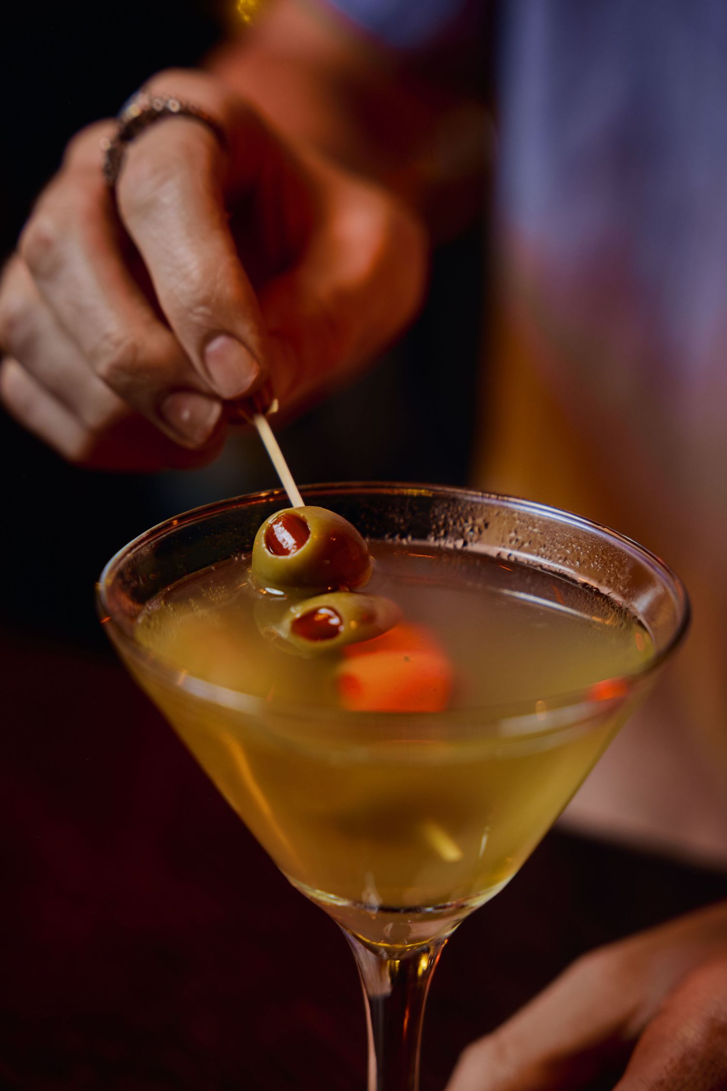 Series of martini cocktails with orange garnishes being served in dimly lit bar setting.