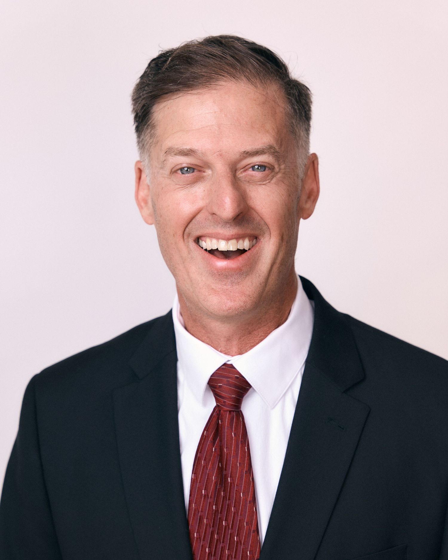 Professional headshots of man in dark suit and red tie showing various expressions.