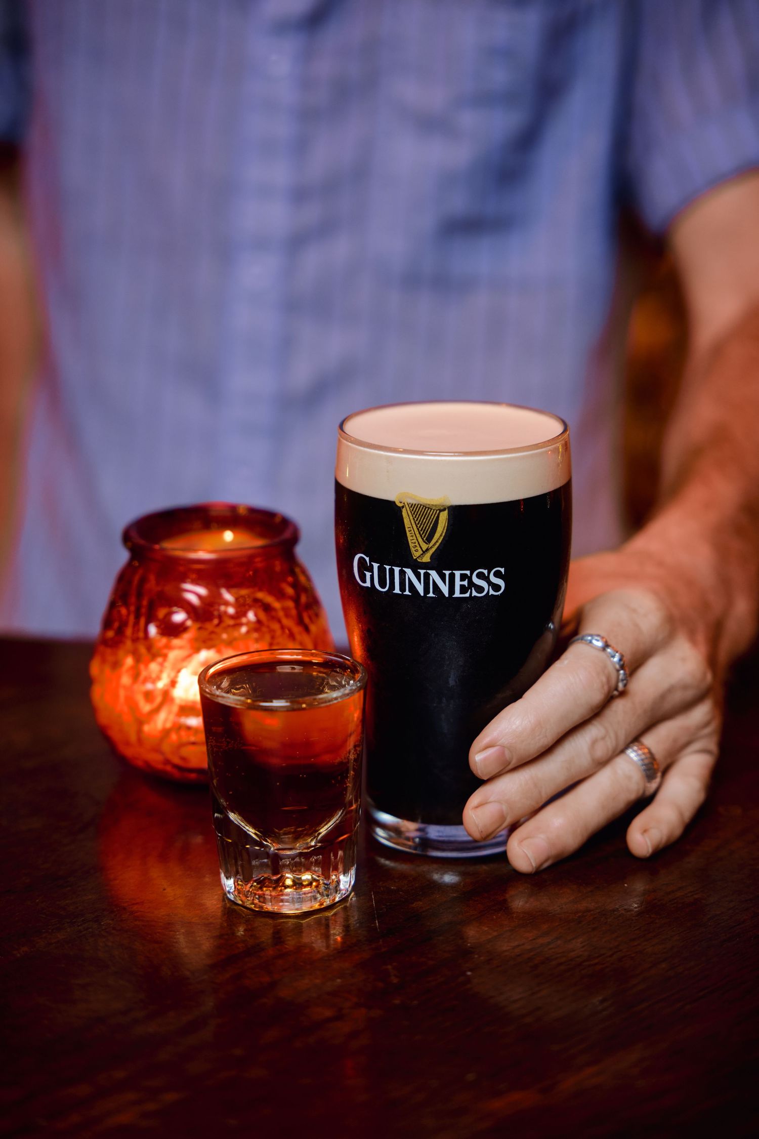 A pint of Guinness beer and shot glass sit on a dark wooden bar beside glowing orange candle holders.