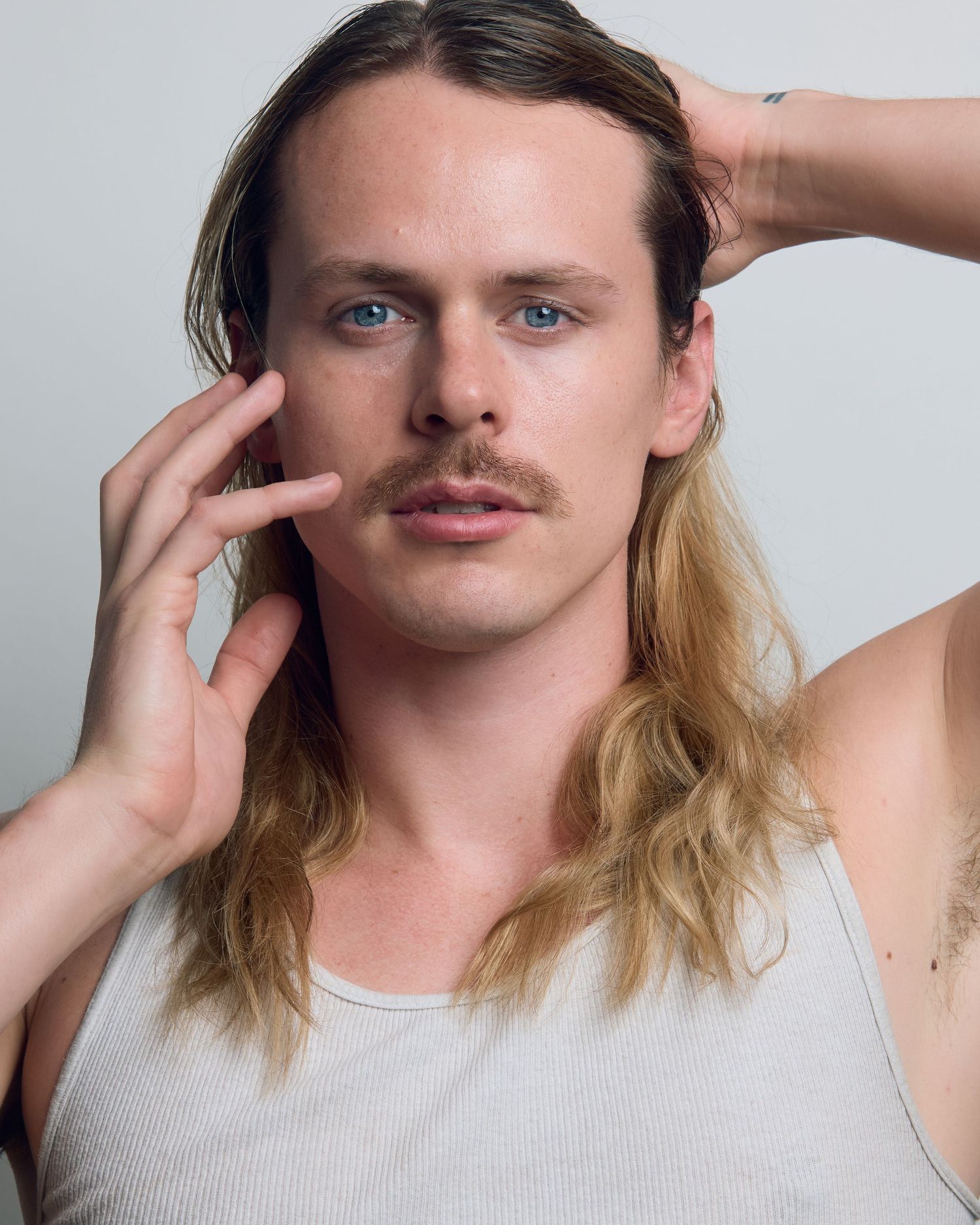 Studio portraits showing long blonde hair and mustache with hands framing face.