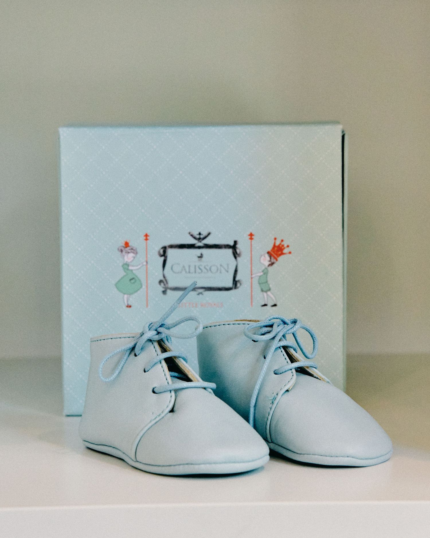 Delicate white baby shoes photographed in a minimalist style against a light background.