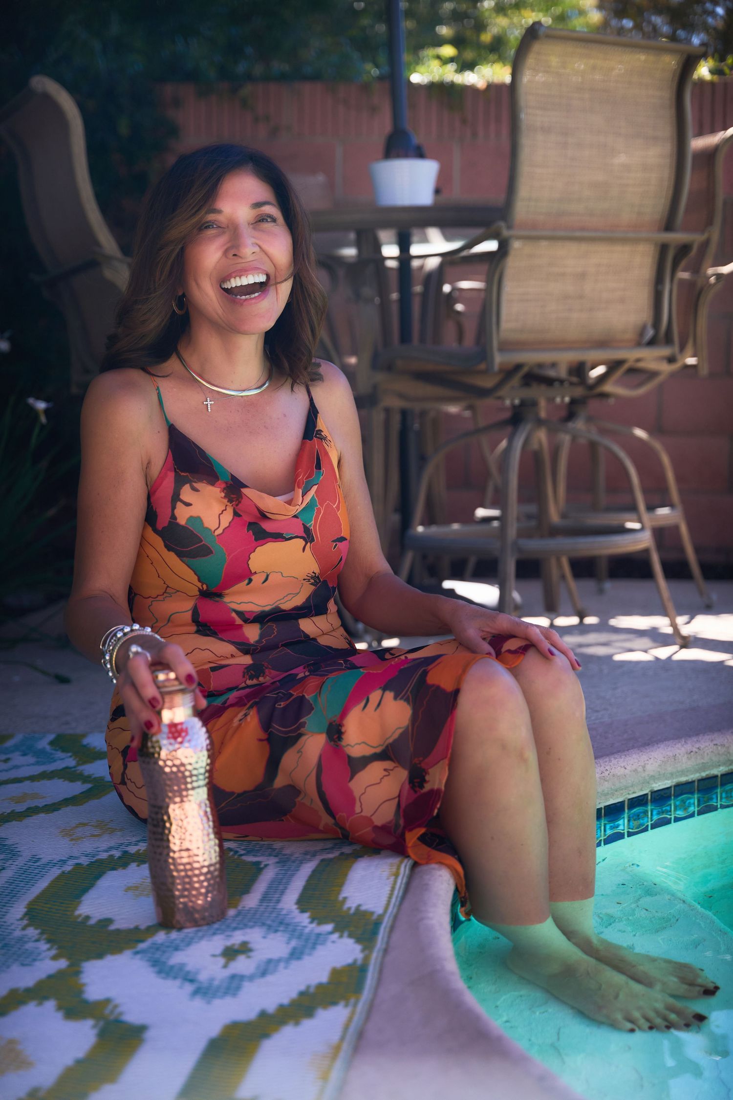 Person in a colorful floral dress sitting by a pool's edge with reflective turquoise water.