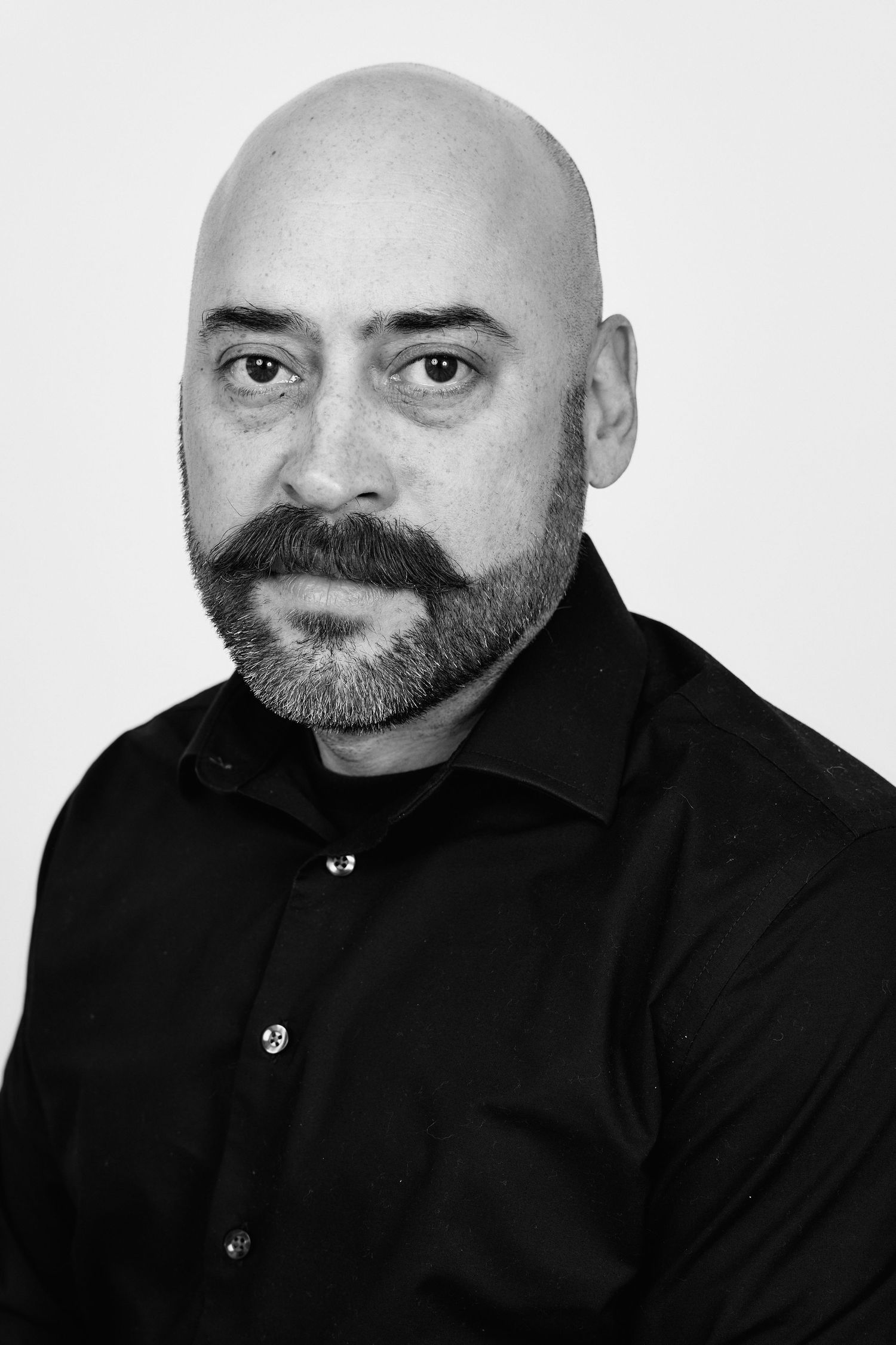 Professional black and white headshot series showing bald man with beard in black shirt against white background.