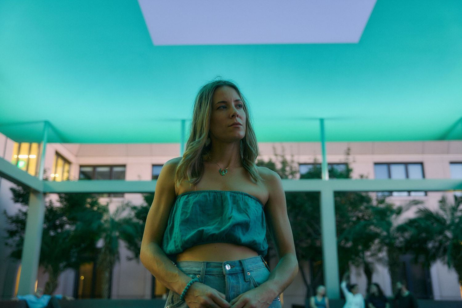 Person in turquoise outfit posing against aqua-colored architectural backdrop.