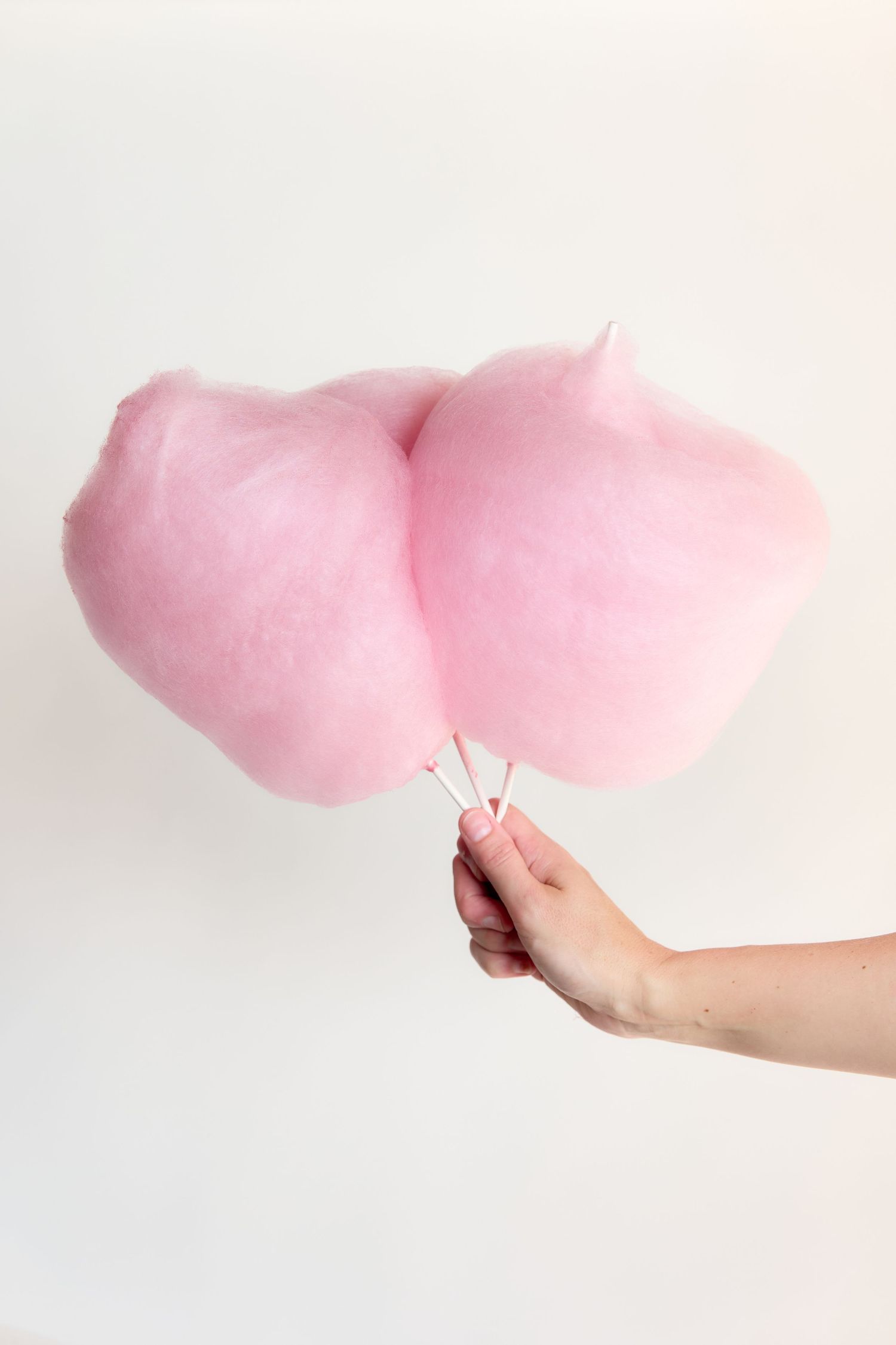 Hand holding two sticks of fluffy pink cotton candy against a white background.