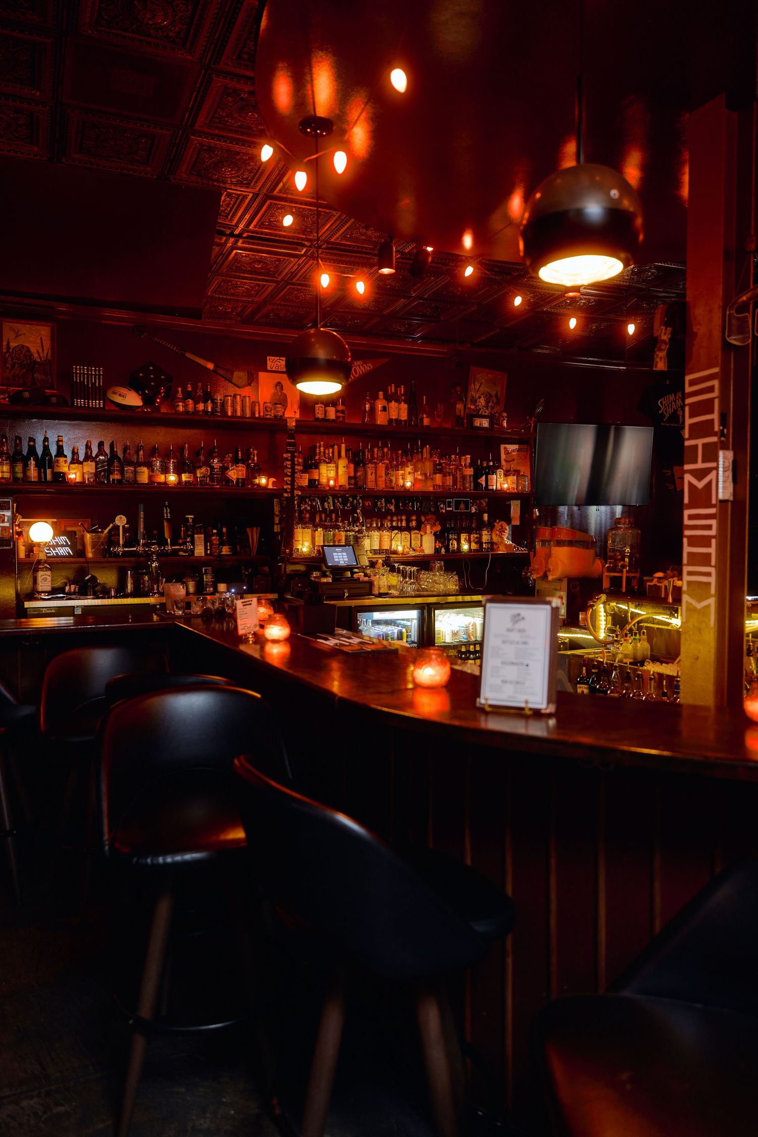 Dimly lit bar interior with warm lighting and rows of liquor bottles behind a wooden counter.