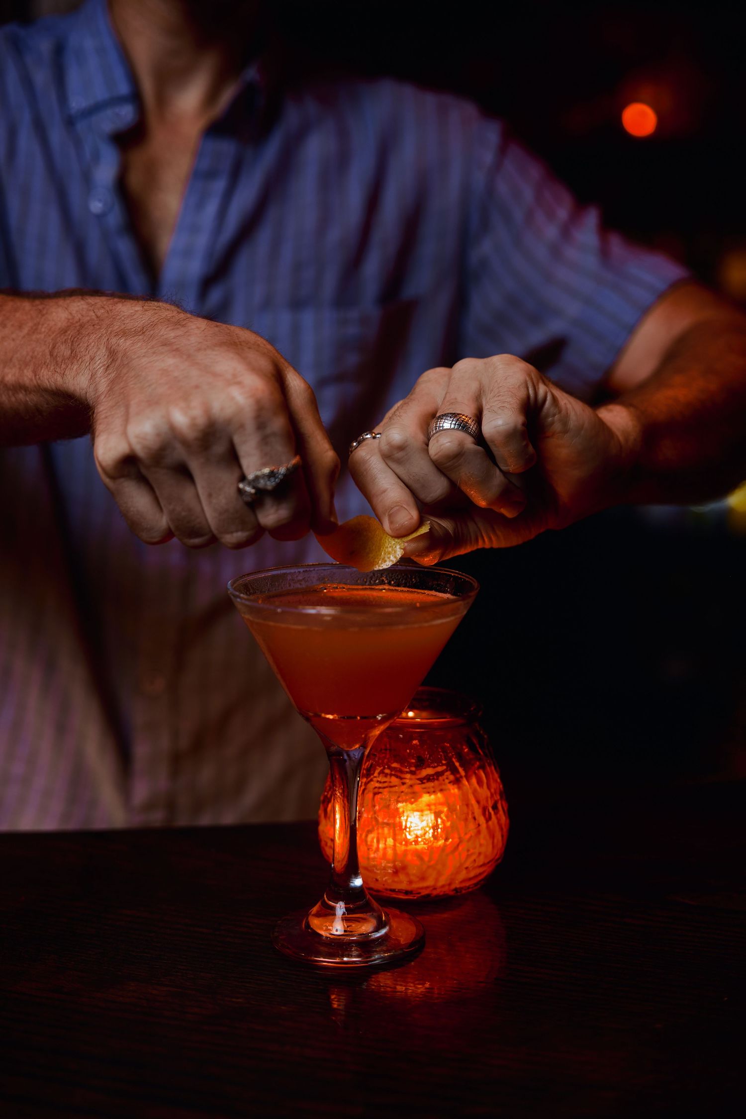 Red cocktail being prepared in martini glass with candlelit ambiance at a bar counter.