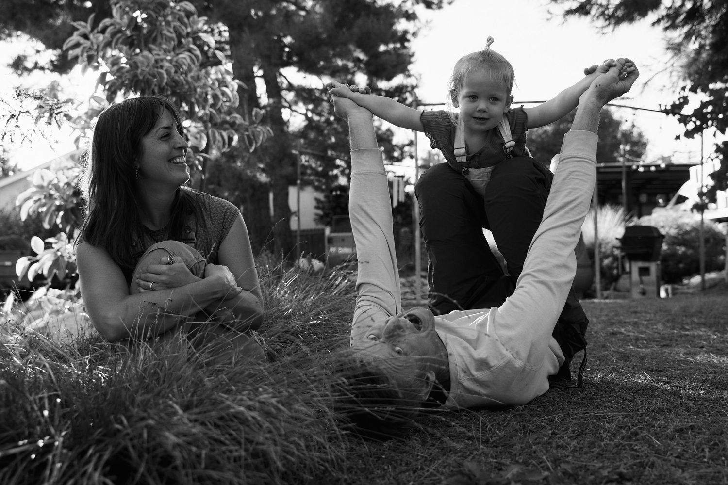 Family lying together on grass in a candid black and white photo sequence.
