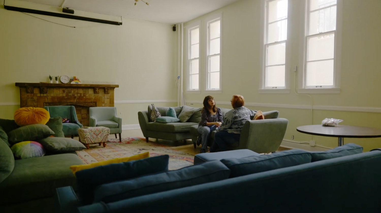 A panoramic view of a modern living room interior with large windows and comfortable seating arrangements.