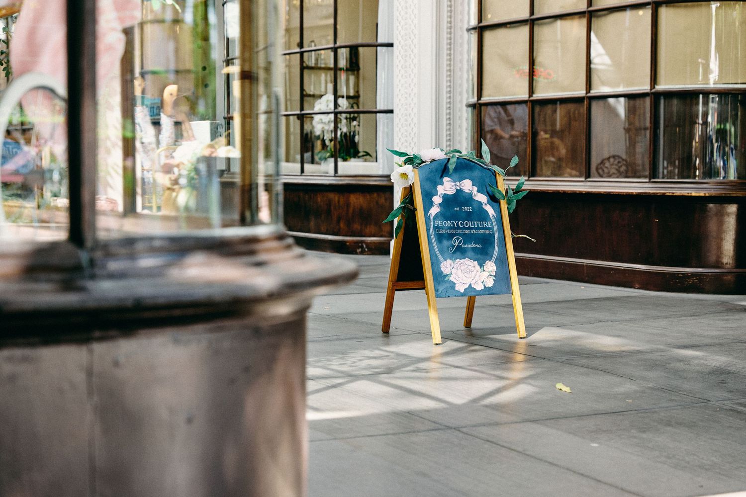 A blue wooden A-frame sign stands on a tiled floor outside a storefront window display.