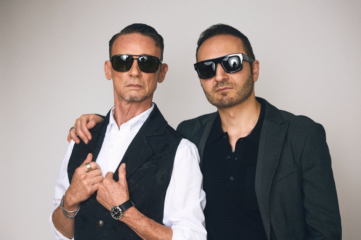 Two people in black suits and sunglasses posing together for dramatic portraits.