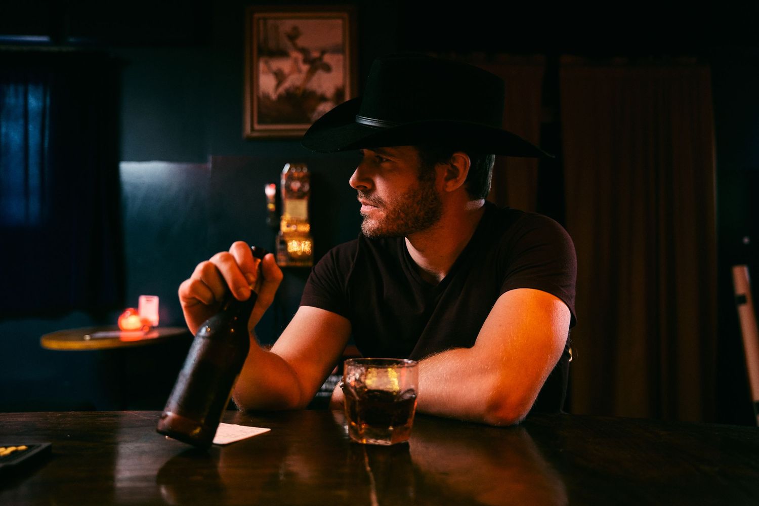 Person holding a glass of beer in a dimly lit bar setting with warm ambient lighting.