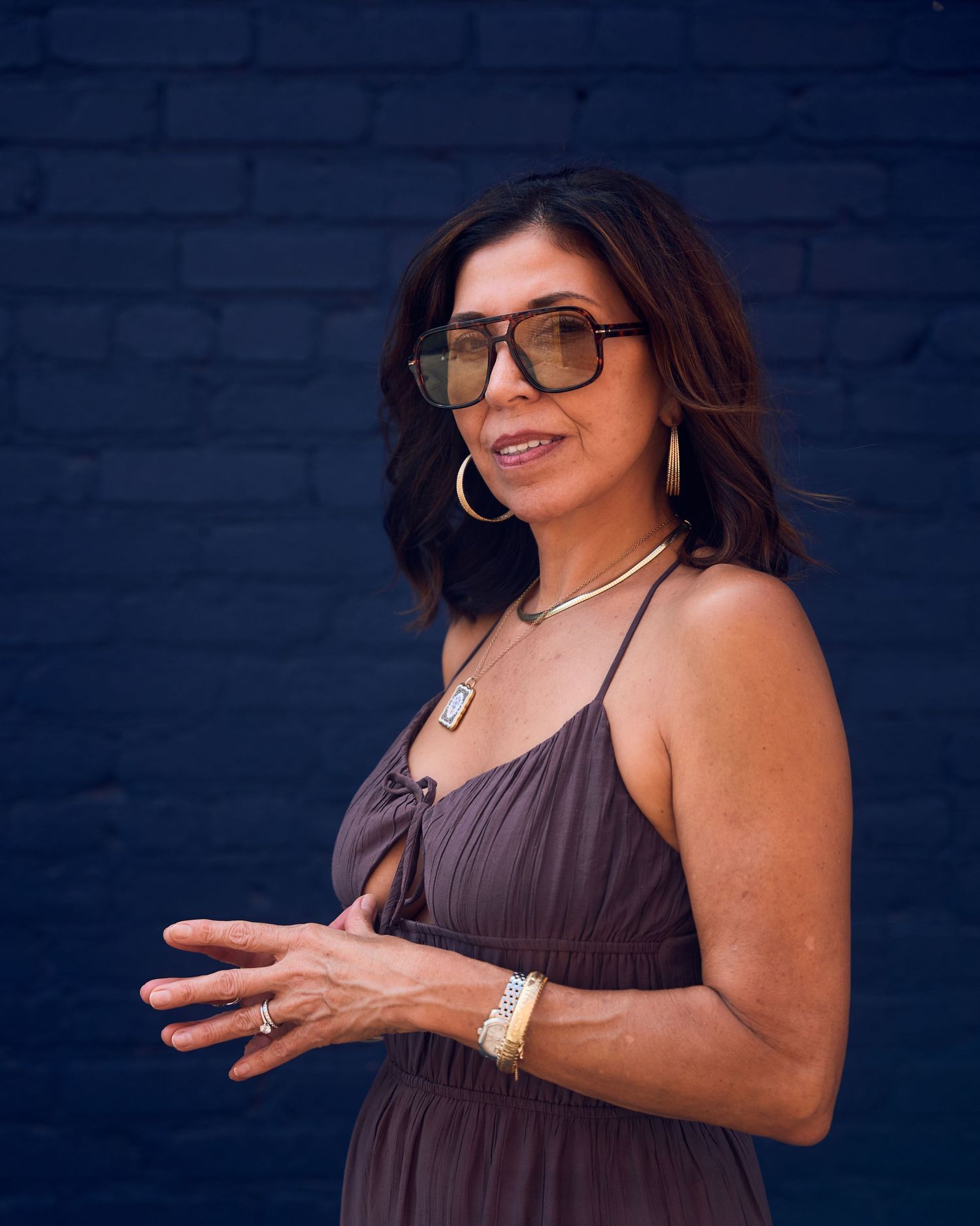 Woman in purple dress gesturing against blue wall background.