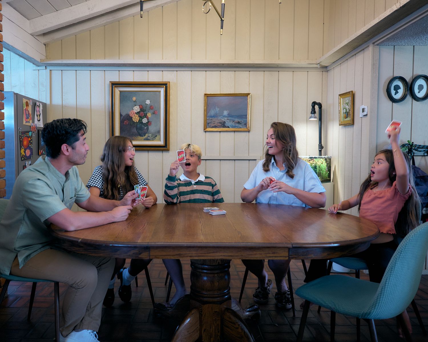 Family members share laughs while sitting around a wooden table in a casual dining room setting.