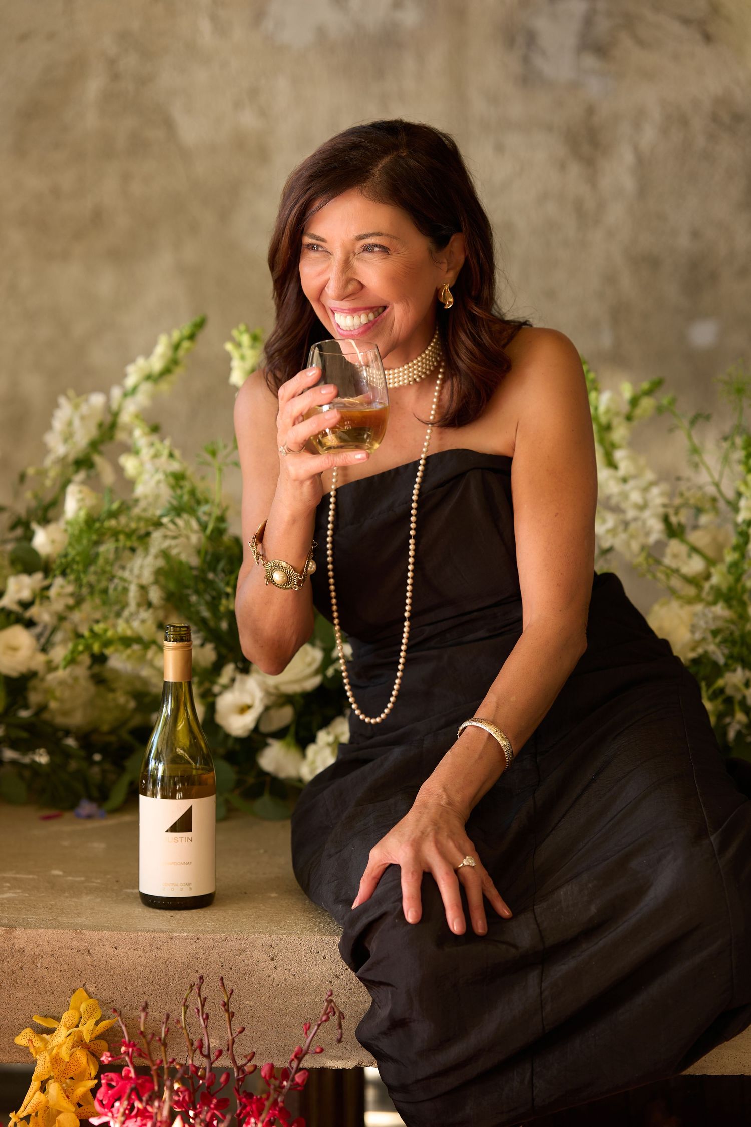 A woman in a black dress poses with wine and flowers in a romantic photoshoot series.