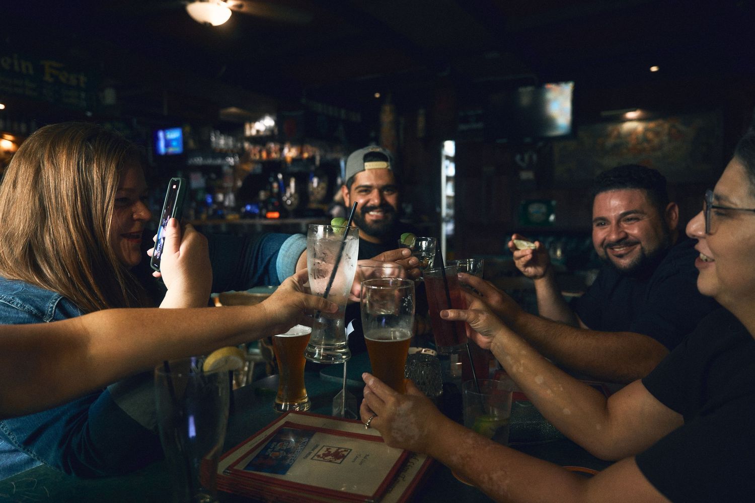 Friends raising glasses and toasting in a dimly lit bar setting.