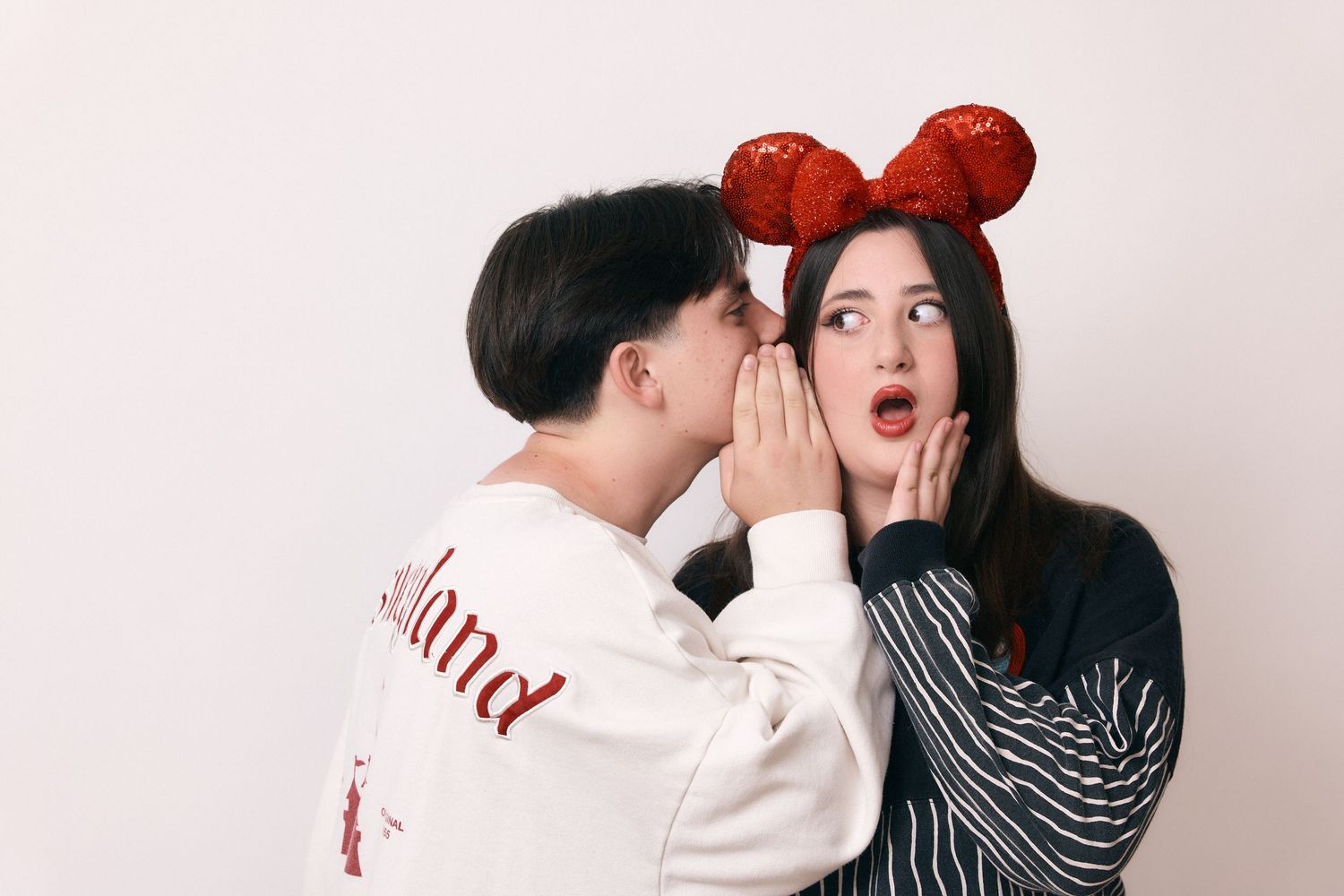 Playful moment captured with Mickey Mouse ears and a surprised expression against white background.