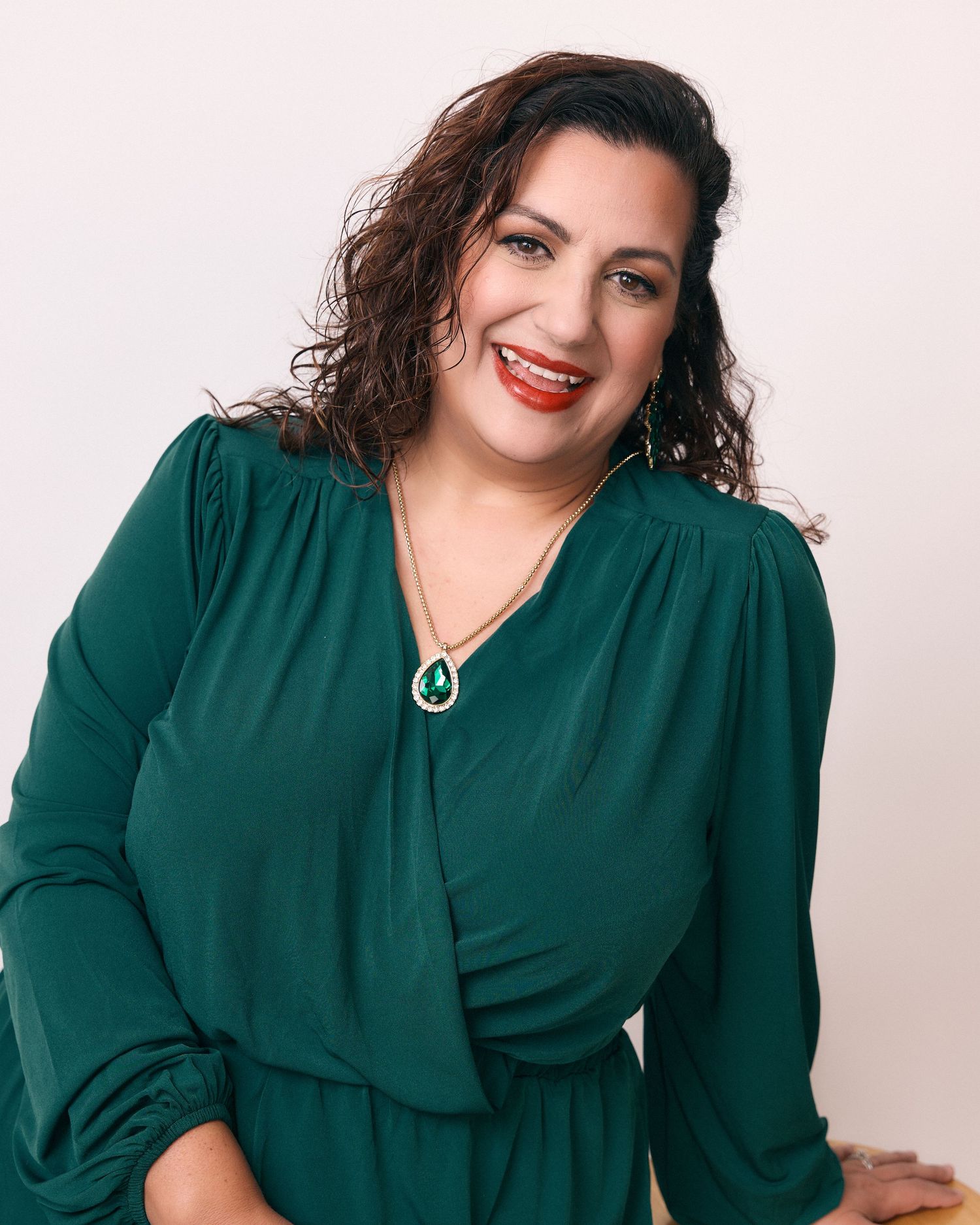 Woman in emerald green dress poses confidently in studio portrait series.