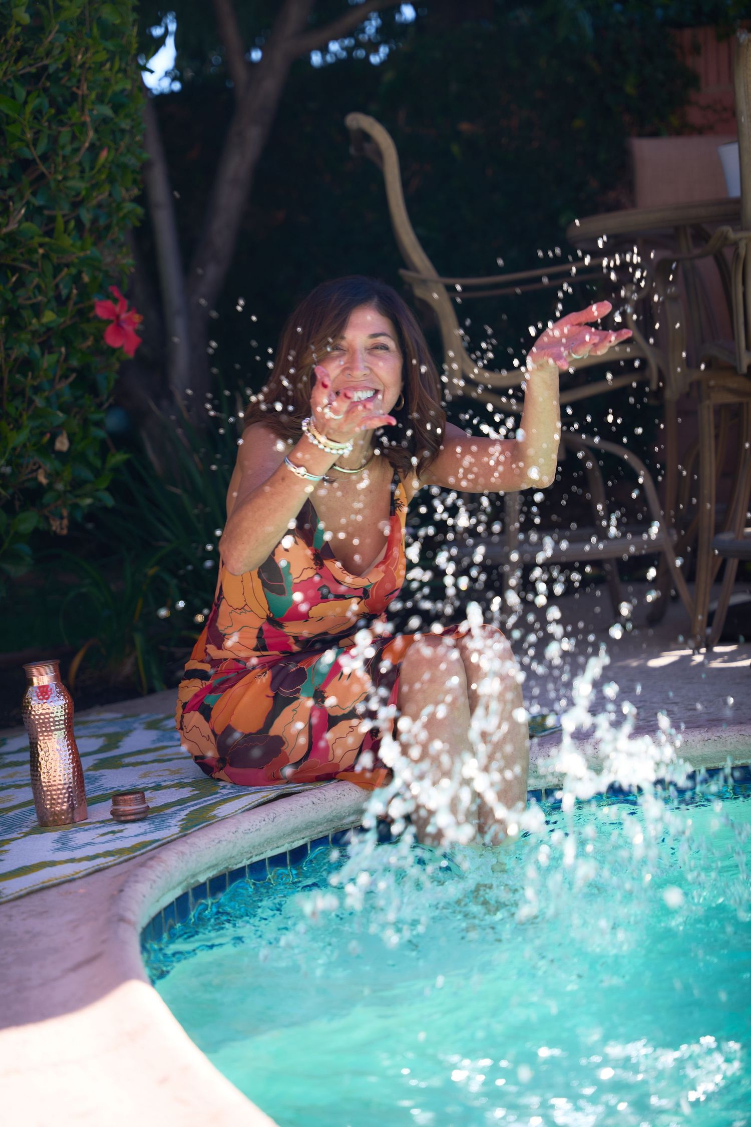 Someone in a colorful dress sits by a pool while water splashes up creating a dynamic summer scene.