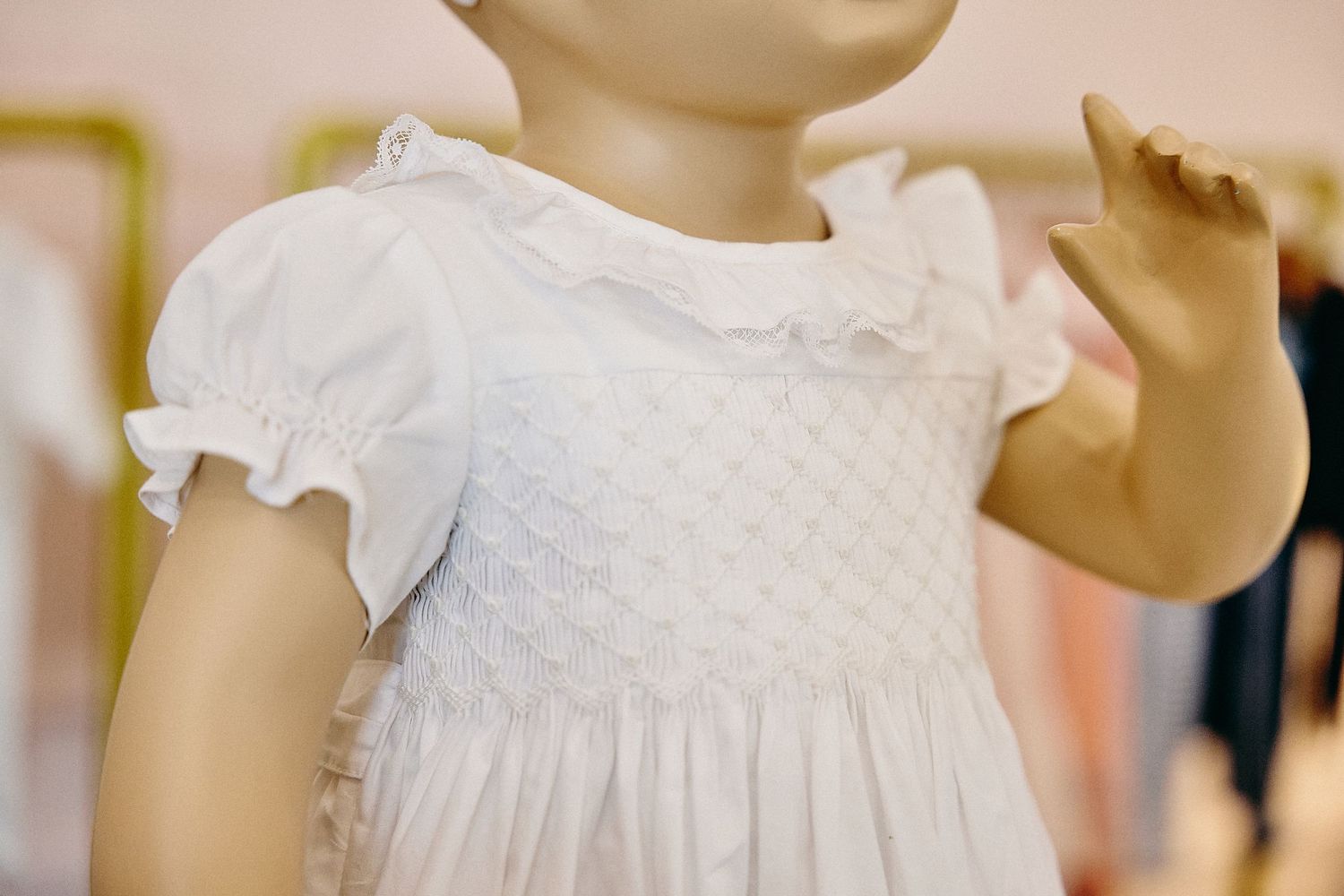 Vintage style white lace christening gowns and baptismal dresses displayed on mannequins in a boutique setting.