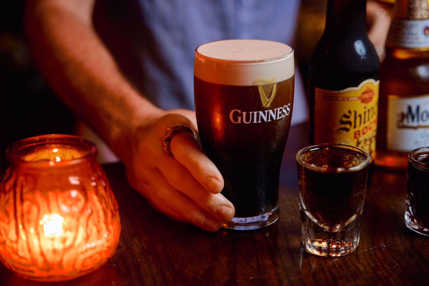 Glasses of dark Guinness beer and lit candles create a cozy pub atmosphere in warm lighting.