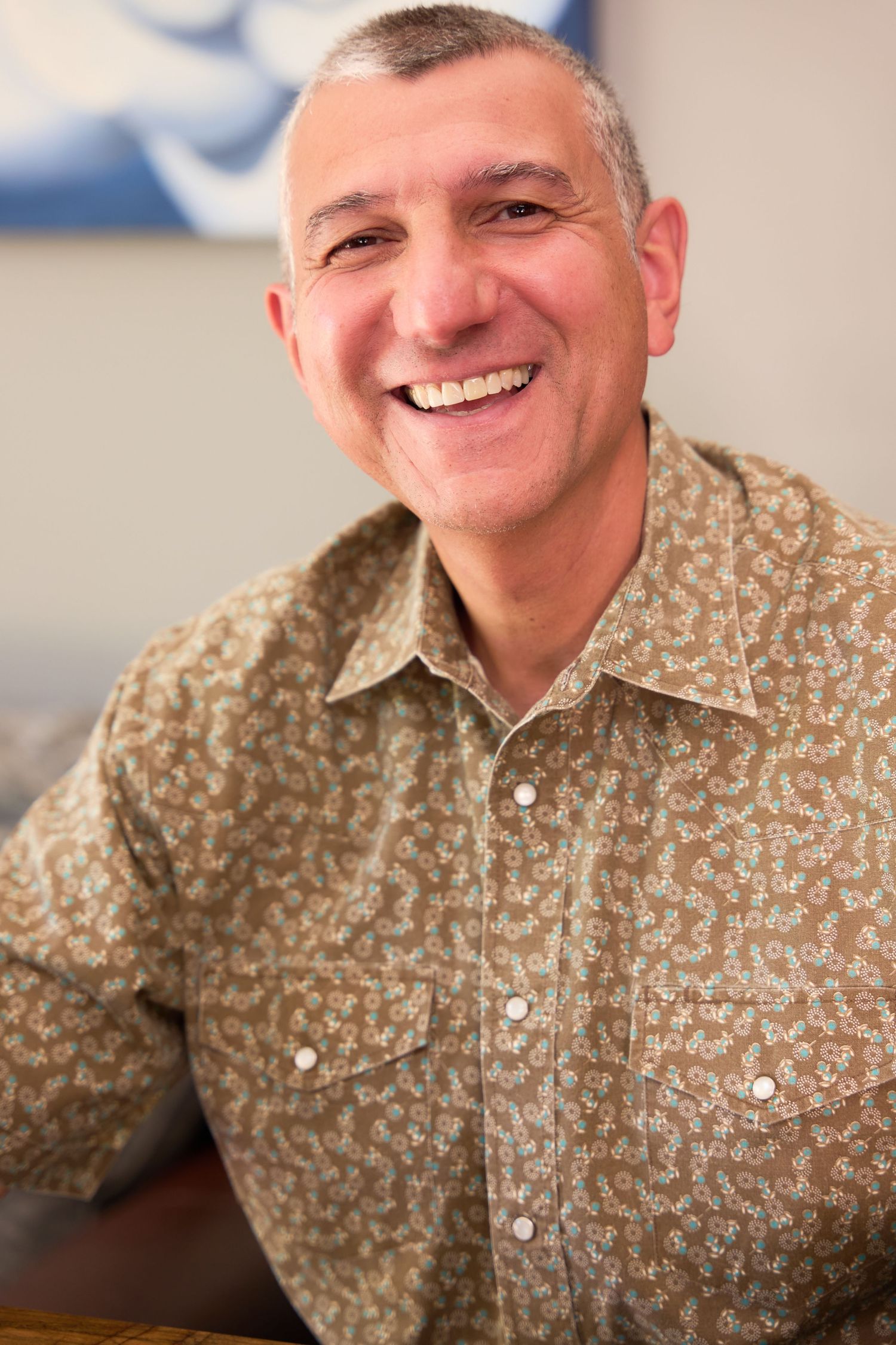 A person in a floral print shirt smiles warmly in a sequence of four similar portrait shots.