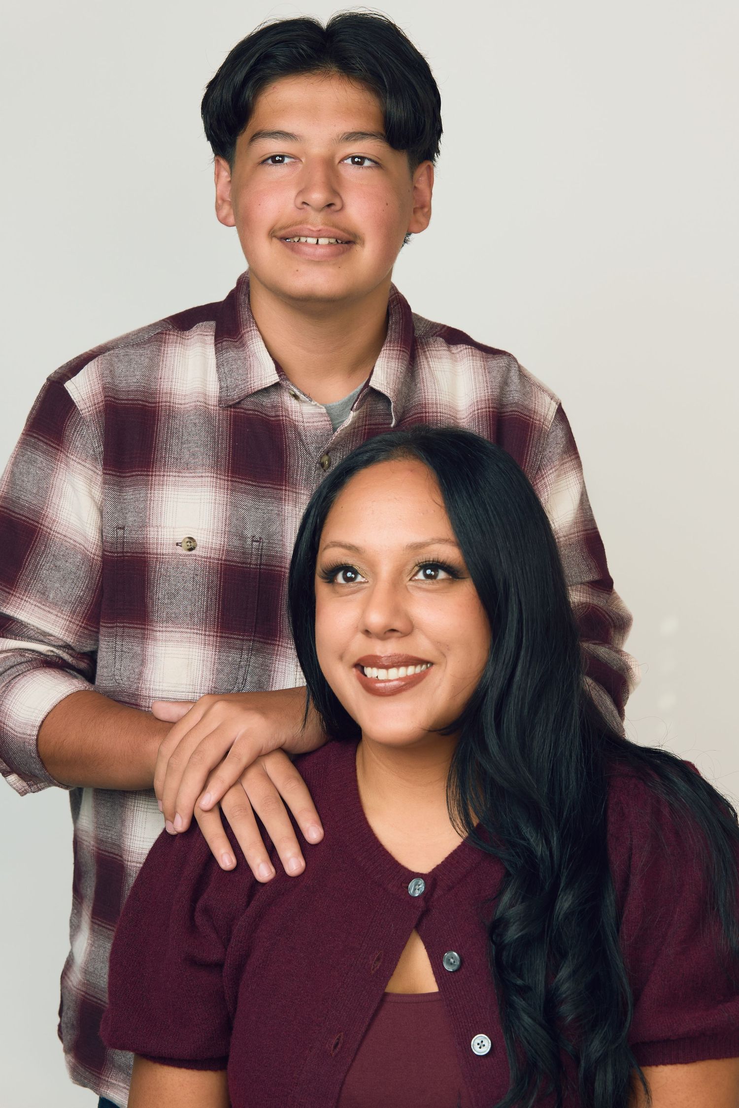 Two smiling young people in maroon outfits pose together for a studio portrait photo.