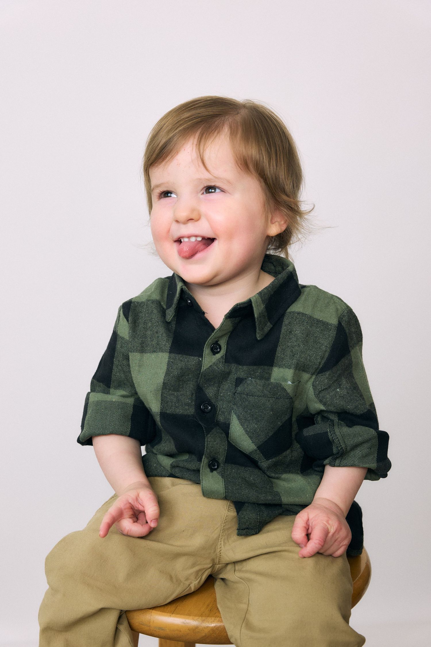 Playful studio portraits of toddler in plaid shirt and khaki pants.