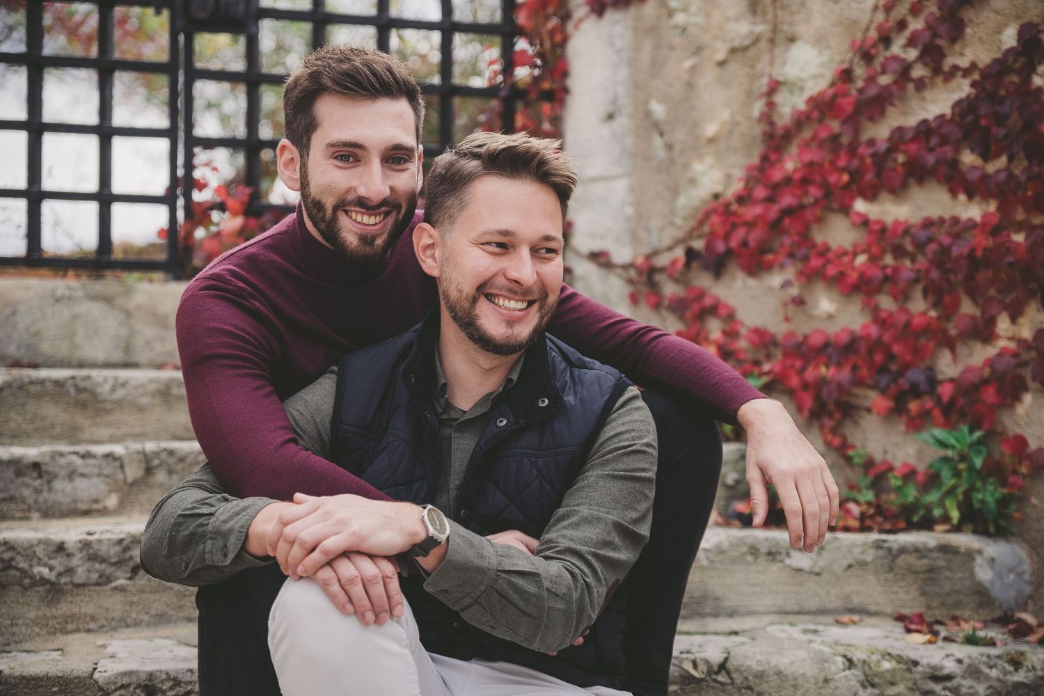 A couple shares intimate moments against a rustic stone wall with red ivy in an outdoor photoshoot.
