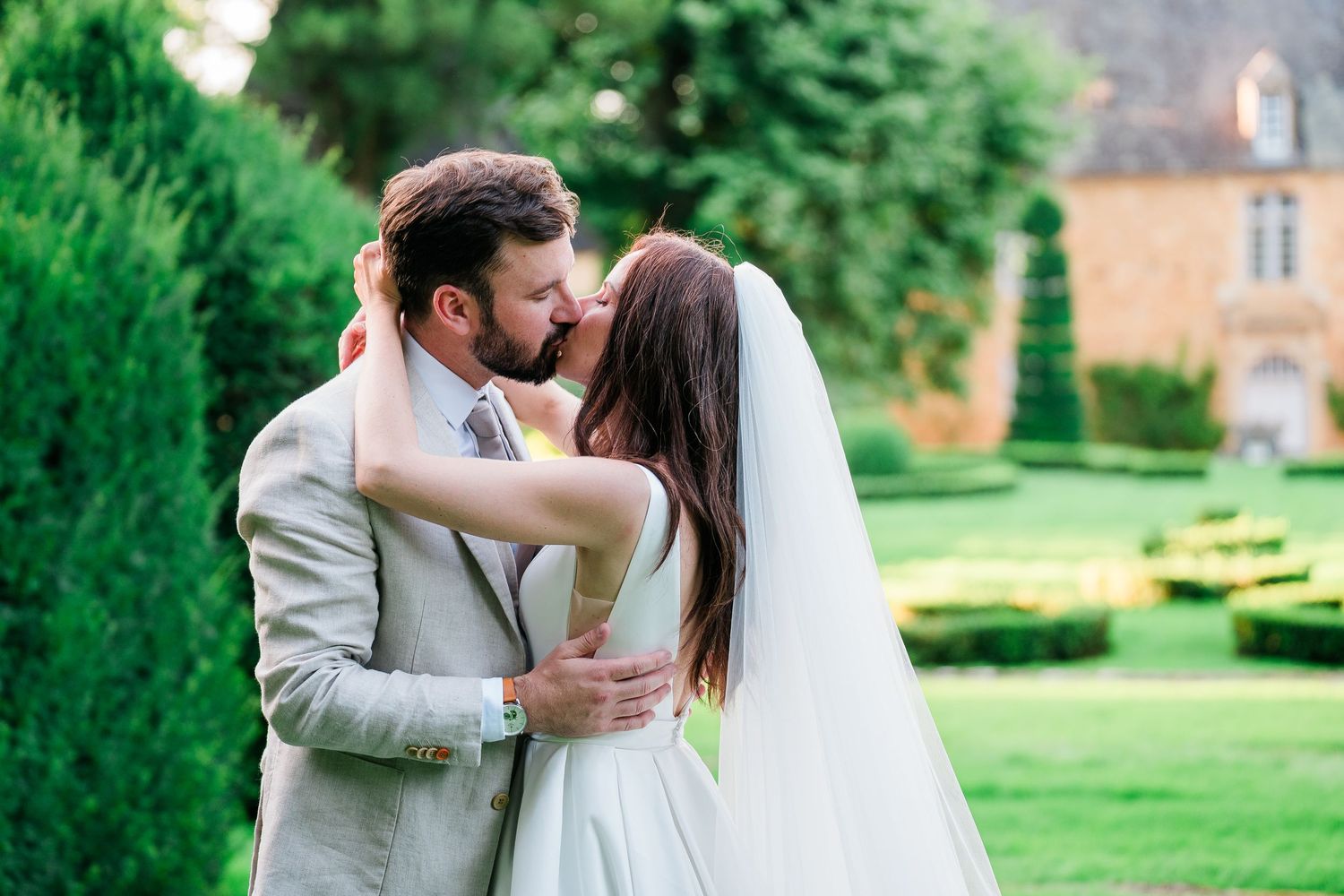 Wedding couple shares intimate moments in a manicured garden with green hedges.