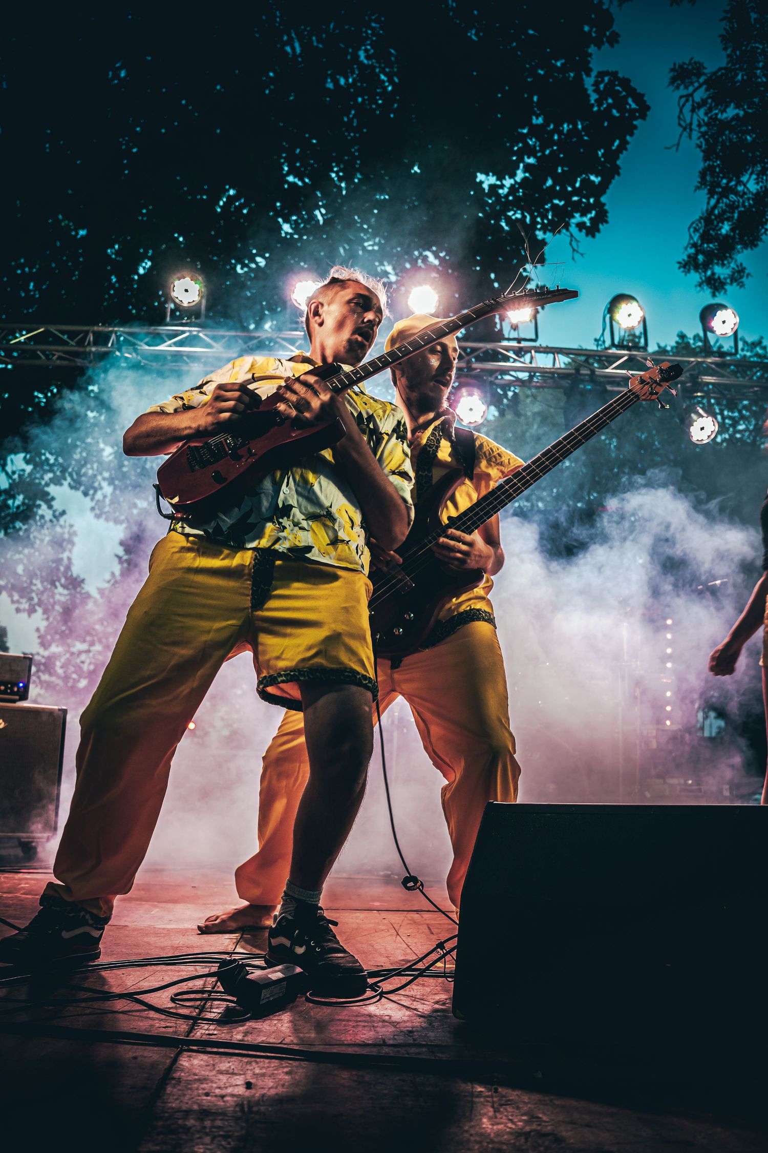 Dynamic low-angle concert shot showing performers in yellow outfits with atmospheric smoke and lighting effects.