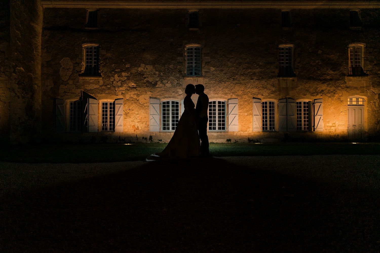 A silhouetted couple stands against an illuminated stone building at night creating a romantic atmosphere.