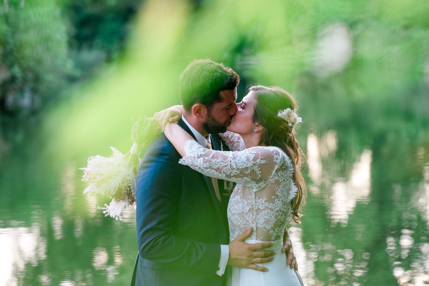 Romantic lakeside wedding portraits with soft focus foliage in foreground.