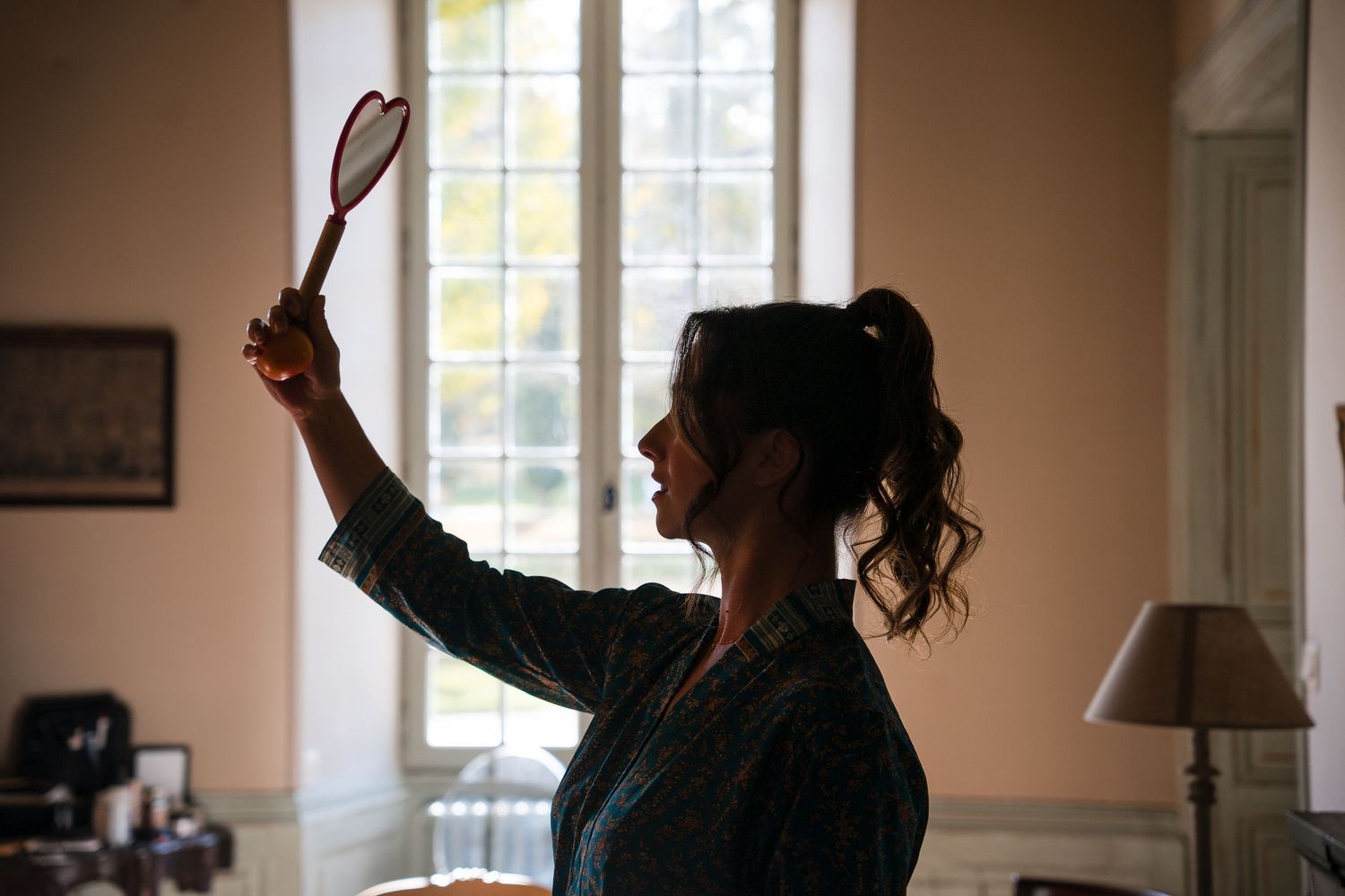 Silhouette of person holding up a tennis racket in a sunlit room with windows.