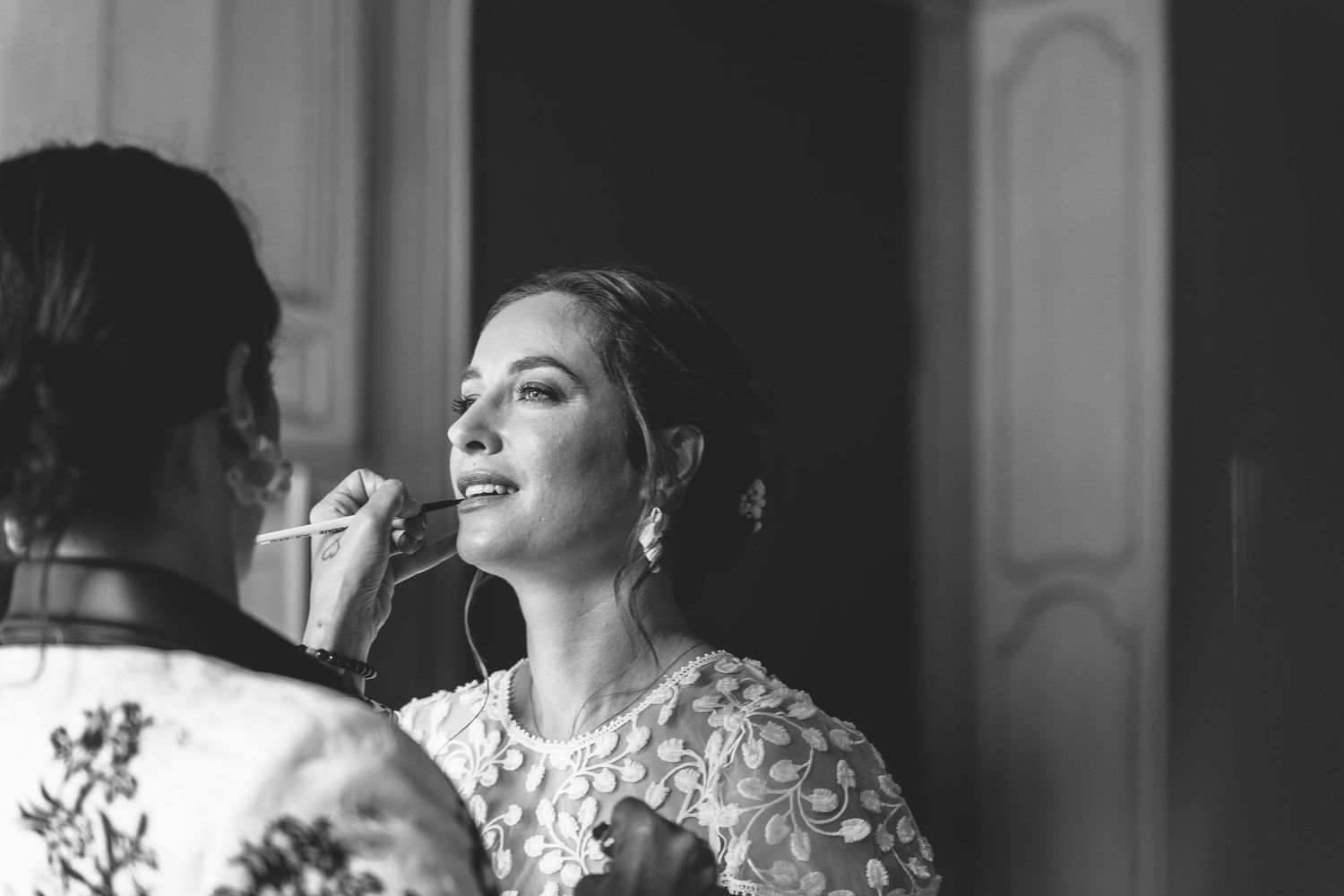 Wedding preparation moment captured in black and white with makeup application.