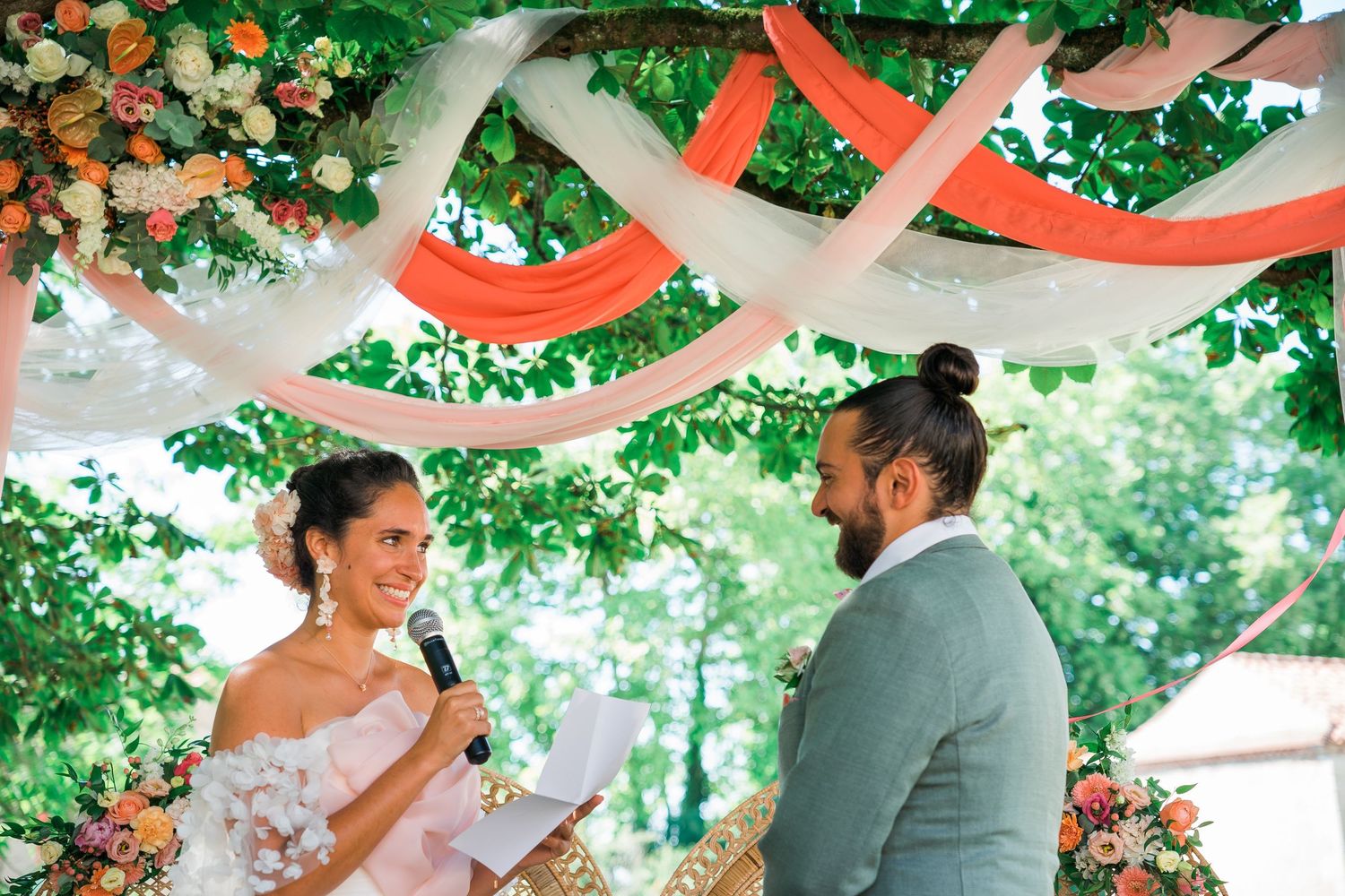 Outdoor wedding ceremony under floral decorations and red fabric draping.