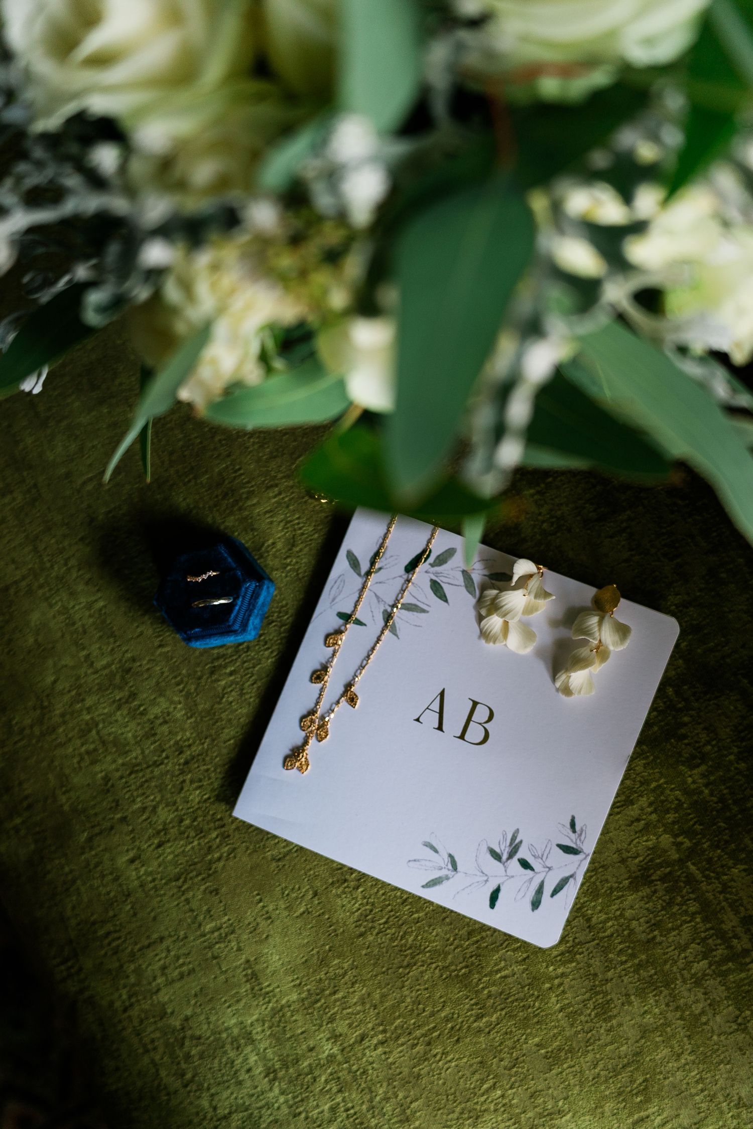 Wedding stationery with floral elements and monogram displayed on dark green surface.