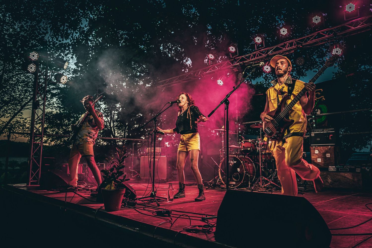 Wide concert stage view with red lighting and silhouetted band members performing live.