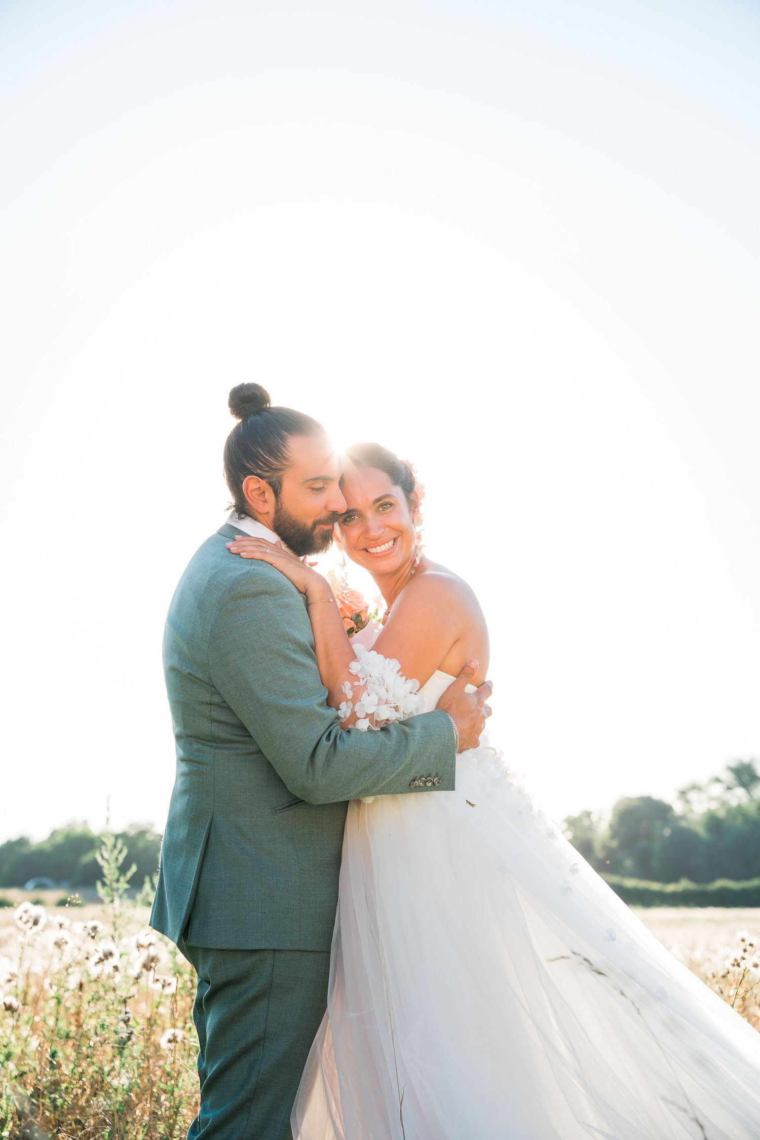 Sunlit wedding portrait of couple embracing in a summer field.
