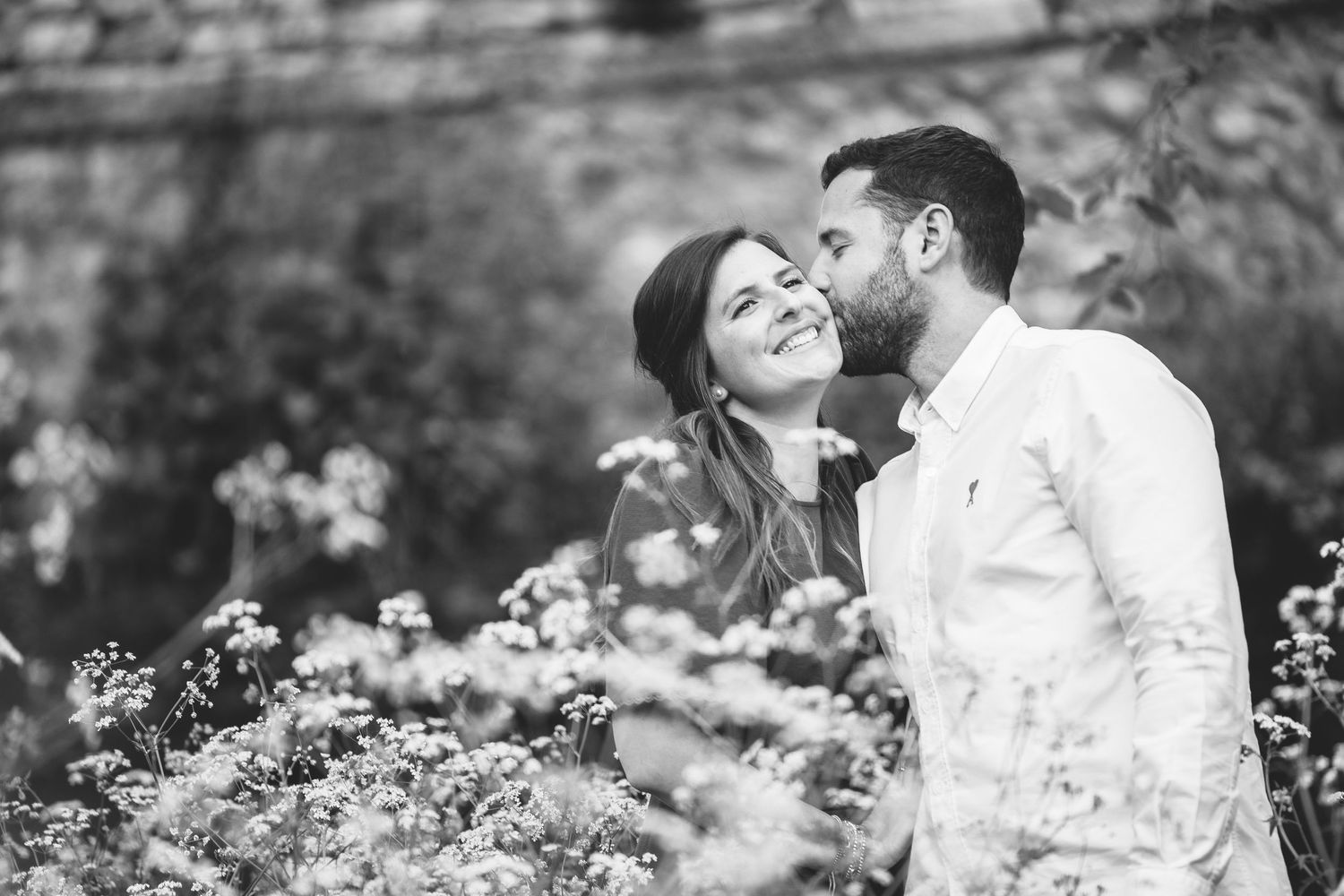 A romantic black and white photo of a couple sharing tender moments among blooming flowers.